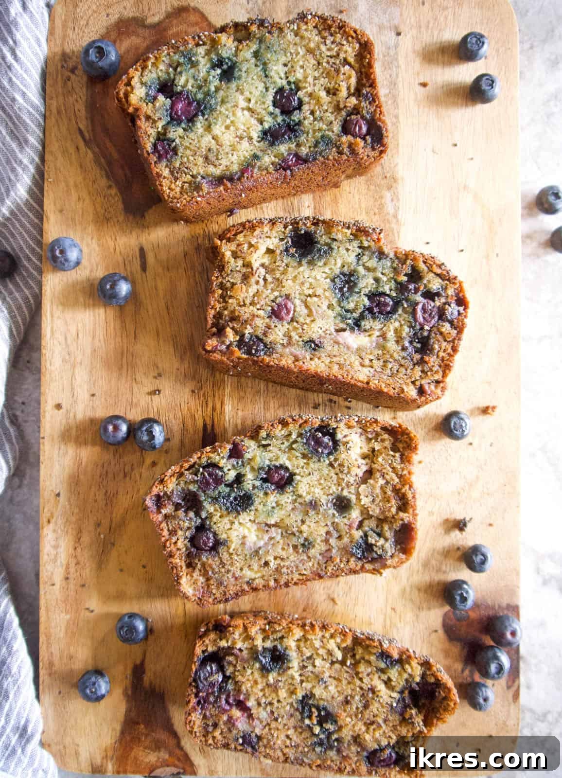 Several slices of blueberry banana bread with Greek yogurt on a wooden cutting board, ready to serve.