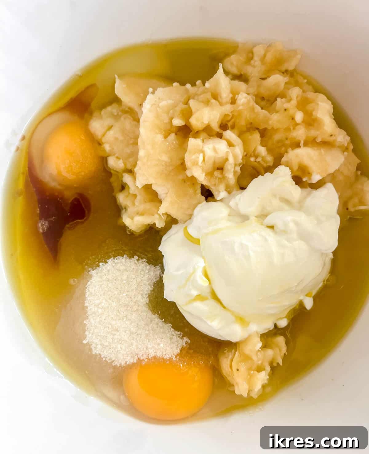 Wet ingredients (olive oil, eggs, mashed bananas, Greek yogurt, sugar, vanilla extract) being mixed in a bowl with a fork.