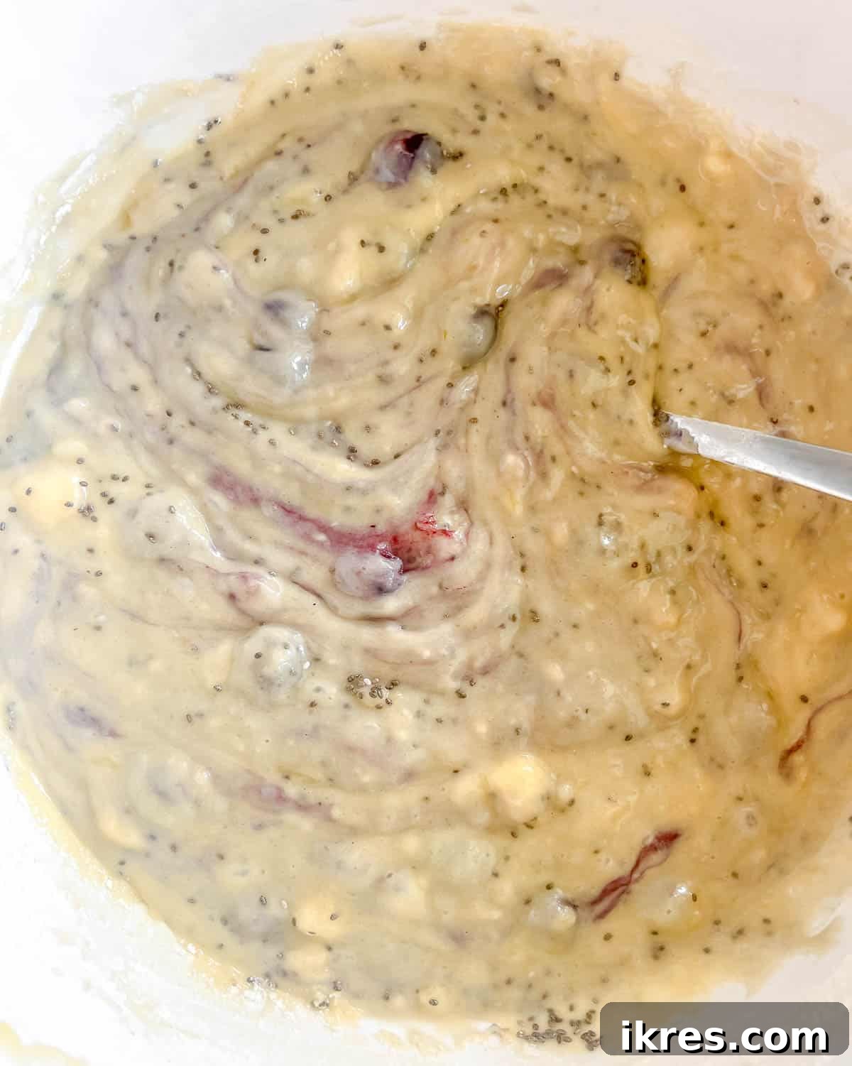 Blueberries and chia seeds being gently folded into the banana bread batter.