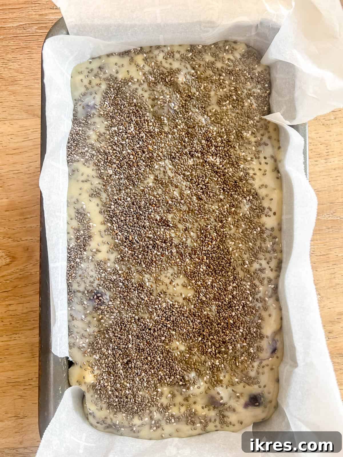 Banana bread batter poured into a greased loaf tin, with chia seeds sprinkled on top.
