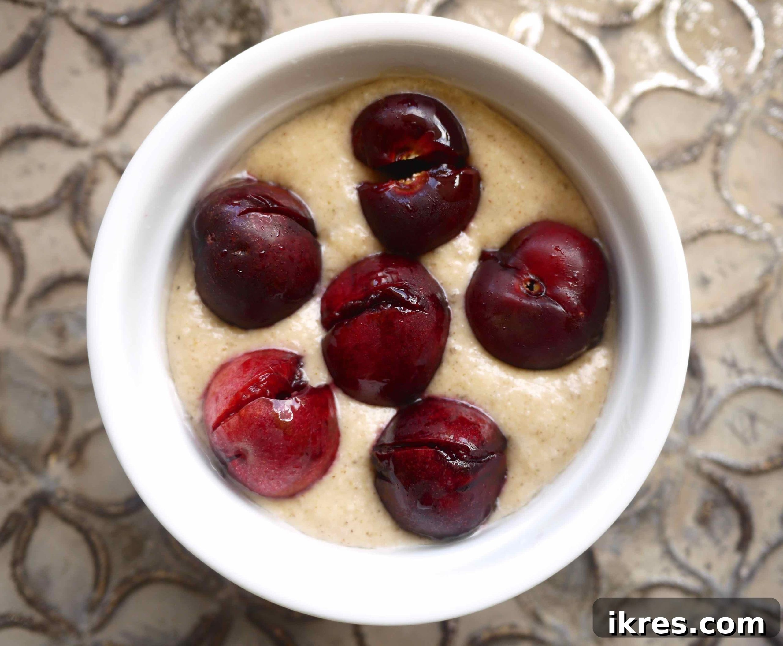 Paleo Gluten Free Cherry Clafoutis 4 Paleo Cherry Clafoutis batter in a ramekin with six pitted cherries pressed into the surface.