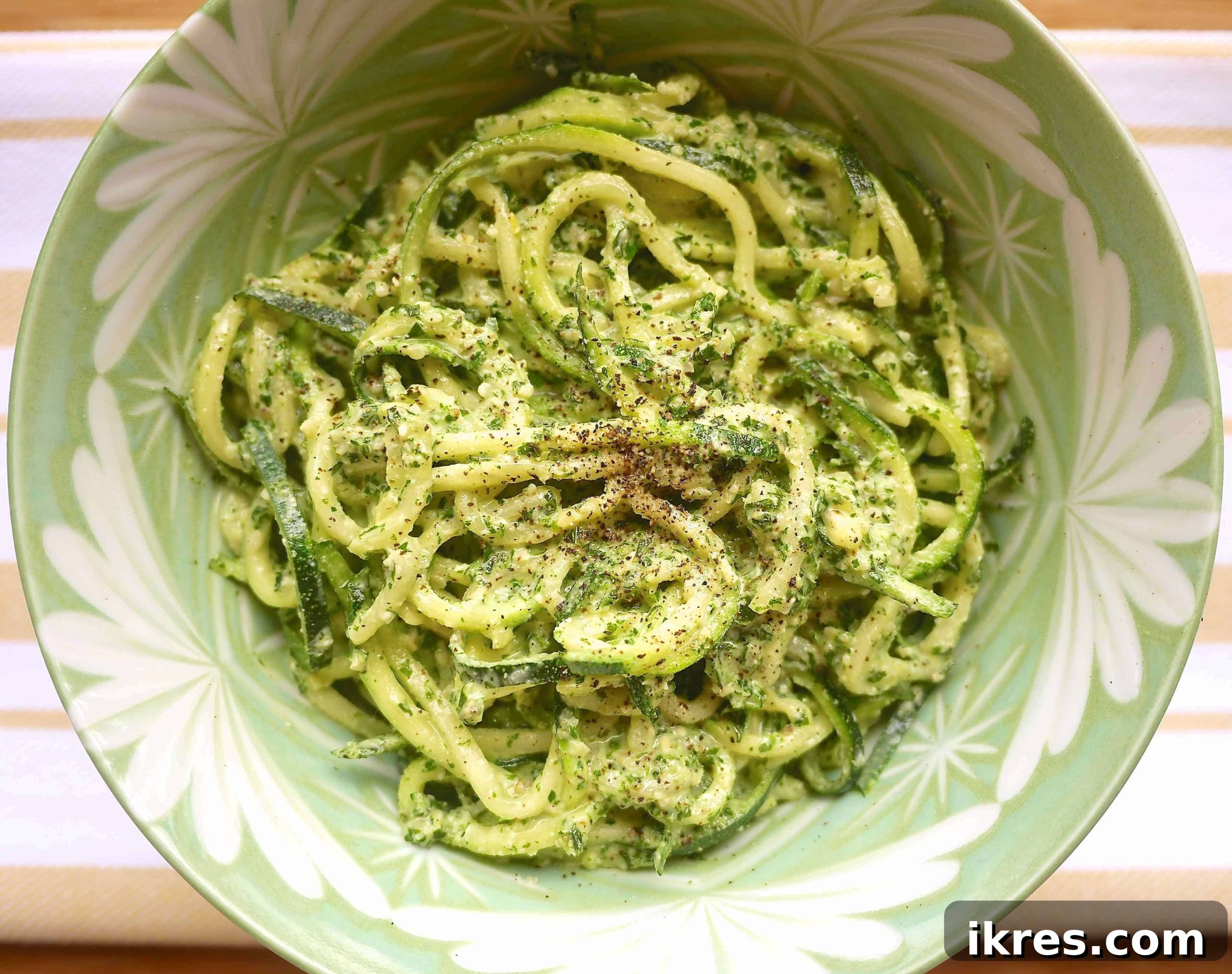 Fresh Zucchini Noodles with Pesto and Kale 2 A bowl of fresh zucchini noodles tossed with bright green kale pesto, garnished with pine nuts and basil leaves, ready to be enjoyed.
