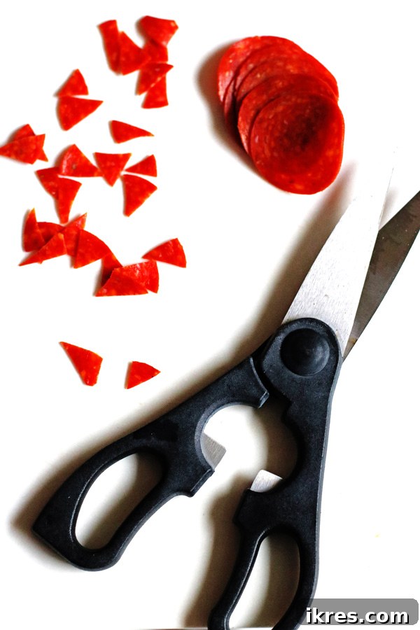 Bewitching Calzone Caps 4 Sliced pepperoni and kitchen shears on a white table. The pepperoni slices are cut into small pieces to use in the calzone recipe.
