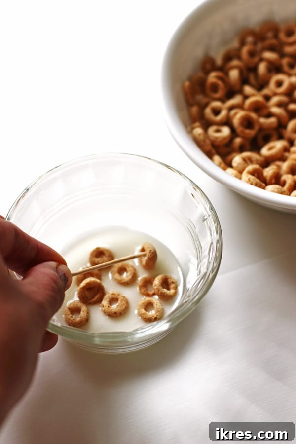 Elven Delights 3 A toothpick is used to dip and coat Cheerios in a bowl of powdered sugar glaze, transforming them into mini Elf Donuts.