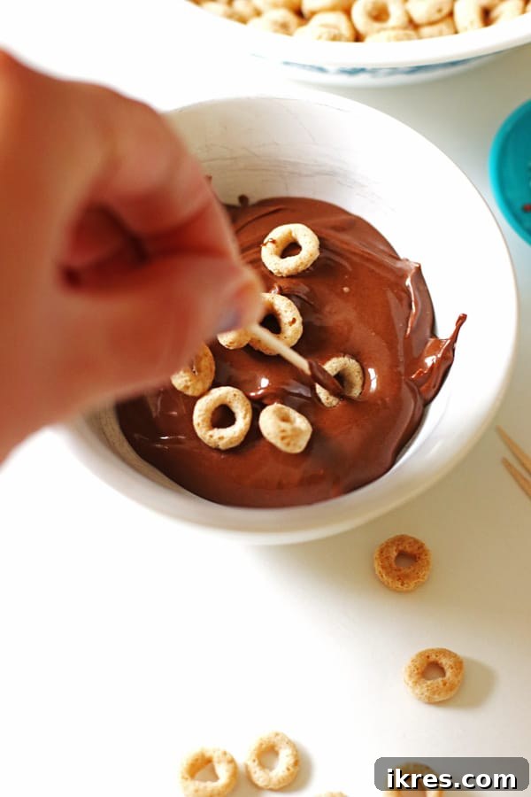 Elven Delights 7 A toothpick is carefully used to dip and fully coat Cheerios in luscious melted chocolate, creating miniature chocolate Elf Donuts.