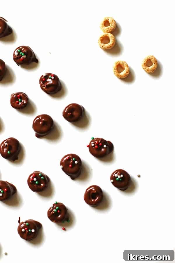 Elven Delights 8 Delicious chocolate-covered Cheerios, festive with red and green sprinkles, cooling and setting on white parchment paper for a holiday treat.