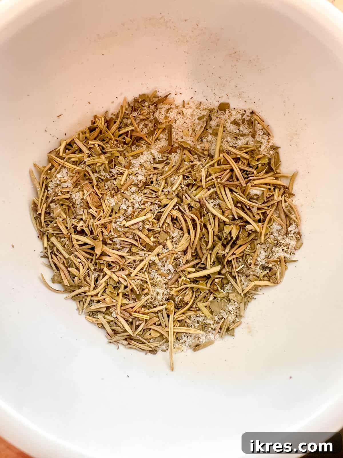 A small bowl holding a meticulously blended mixture of salt, pepper, dried rosemary, thyme, basil, and oregano, ready to season the chicken.