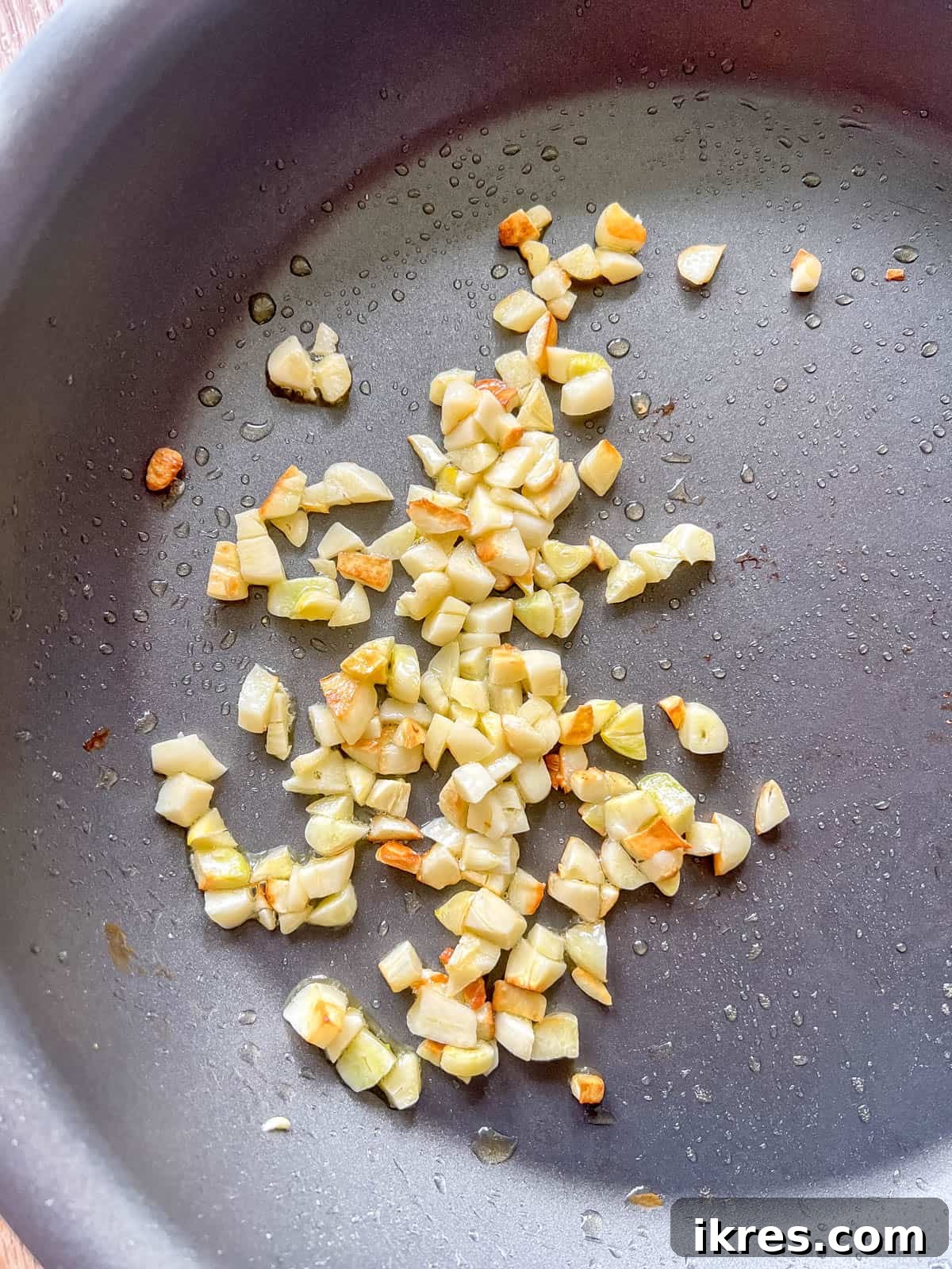 Bursting Cherry Tomato Garlic Sauce 4 Freshly chopped garlic cloves gently sautéing in shimmering olive oil in a pan, releasing their aromatic fragrance.