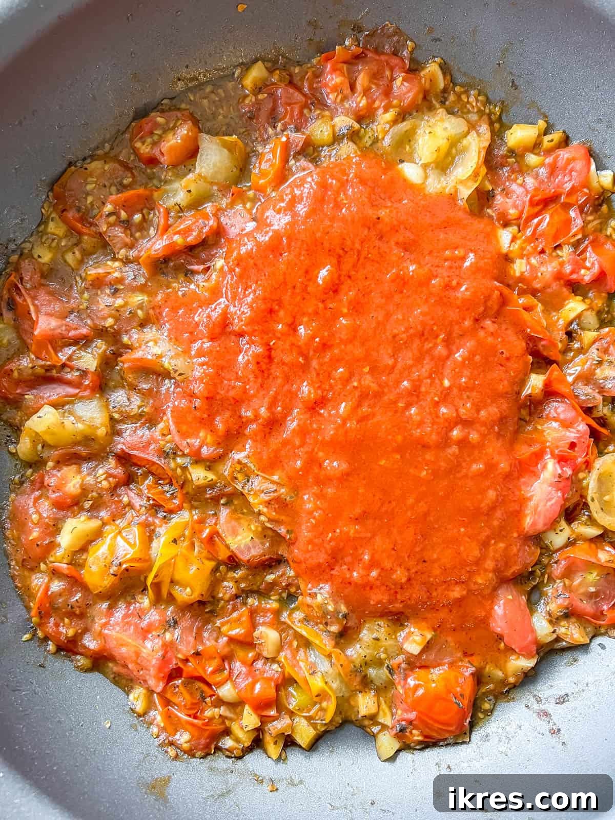 Bursting Cherry Tomato Garlic Sauce 6 Cooked cherry tomatoes being gently mashed in a pan with a potato masher to release their flavorful juices and create a chunky sauce.