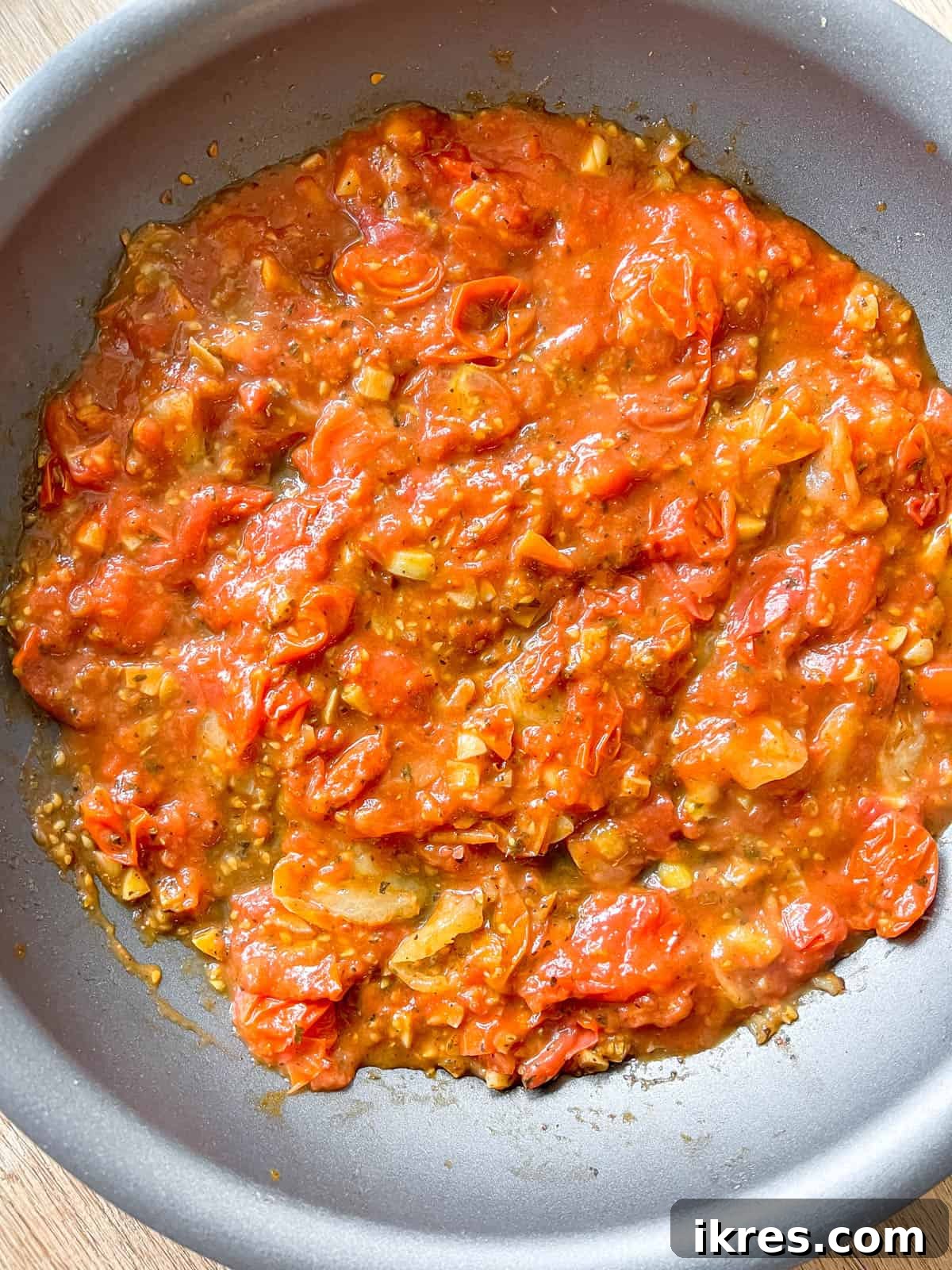 Bursting Cherry Tomato Garlic Sauce 7 Marinara sauce being poured into the pan with the cooked cherry tomatoes and spices, ready to be mixed into a unified sauce.