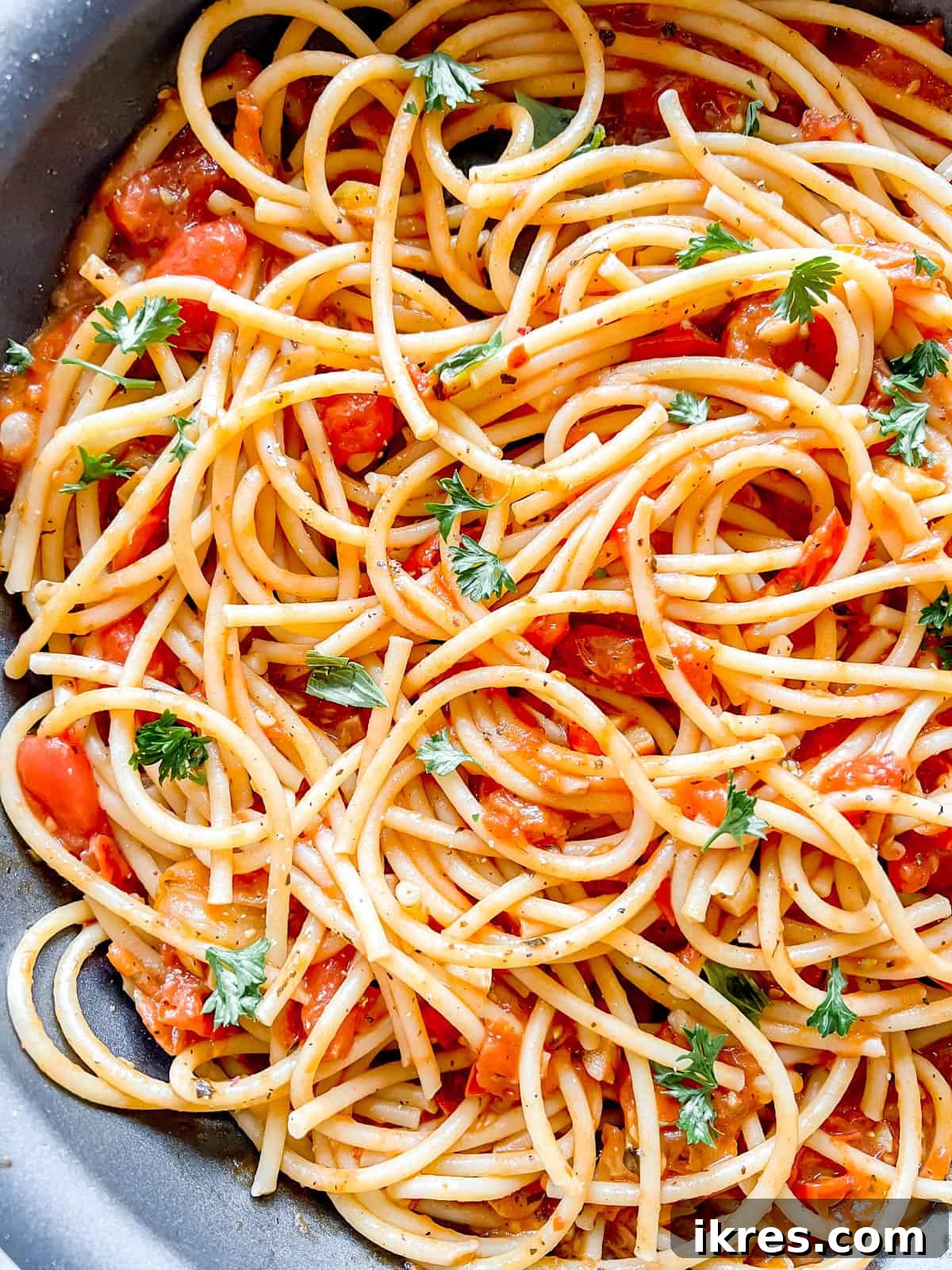 Bursting Cherry Tomato Garlic Sauce 8 The vibrant cherry tomato and garlic sauce being mixed into cooked pasta directly in a large pan, making it ready to serve immediately.