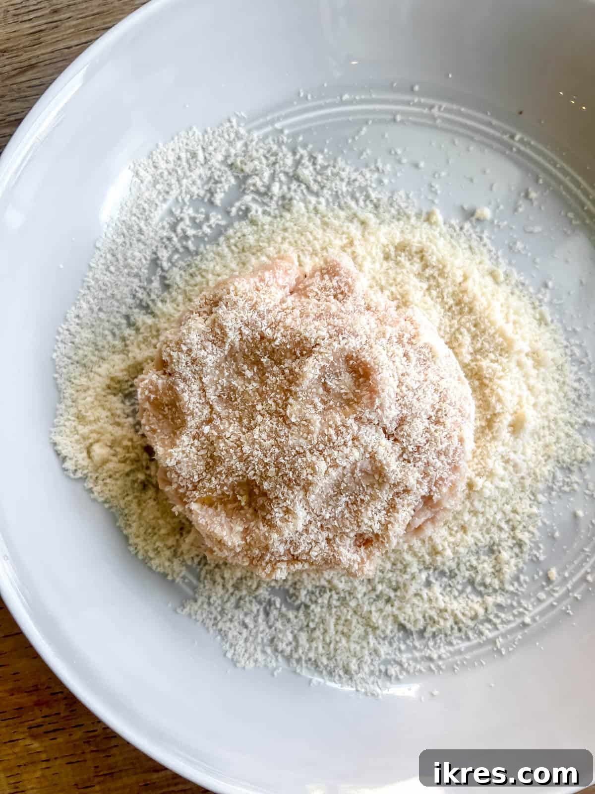 A chicken burger patty being dunked in almond flour to create a light coating.