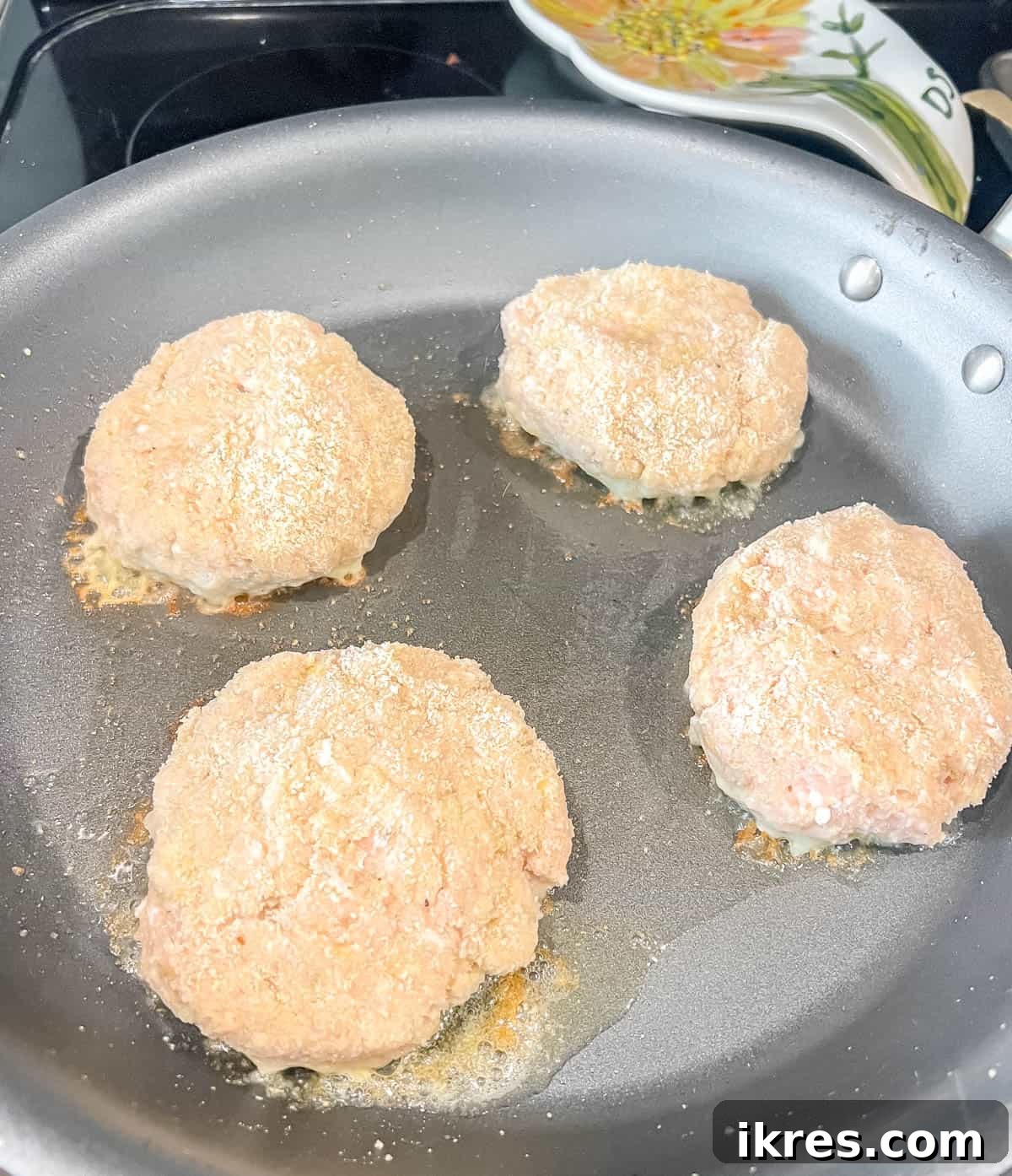 Chicken burgers sizzling in a pan over medium heat.