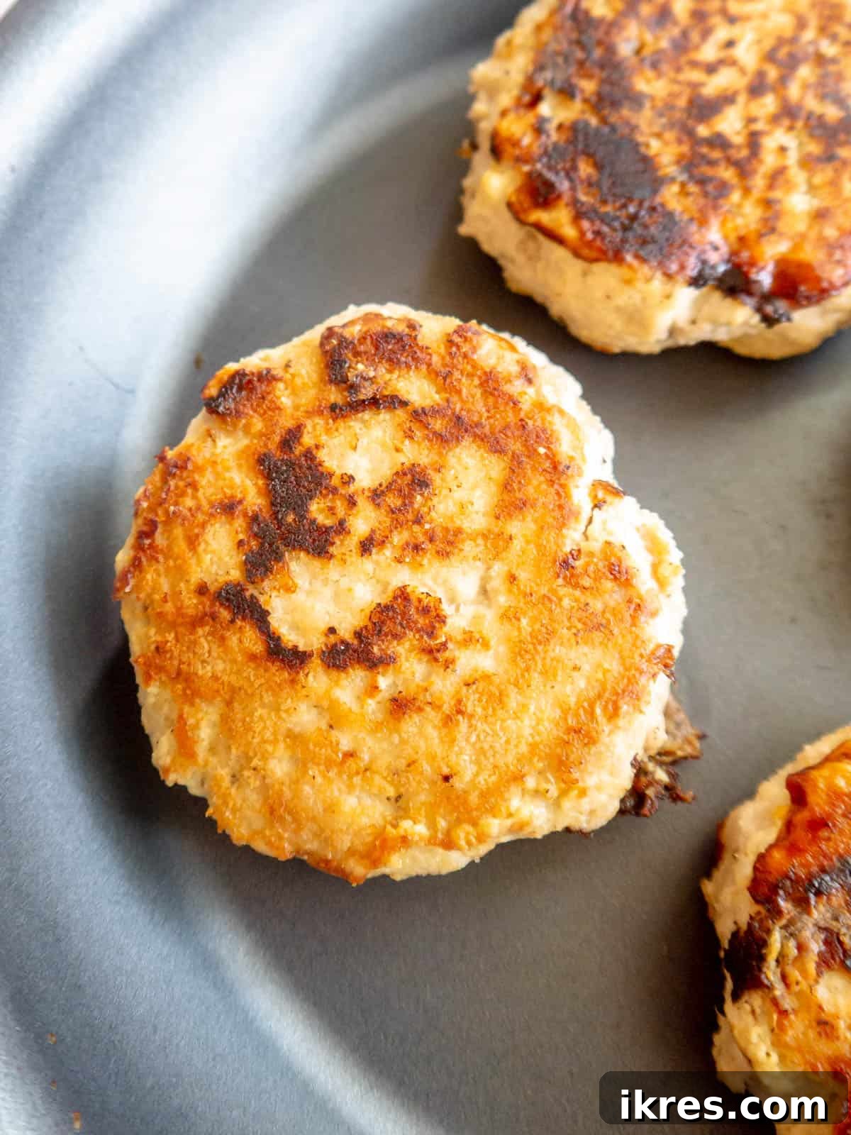 A perfectly golden-brown chicken burger patty cooked on a frying pan, ready to serve.