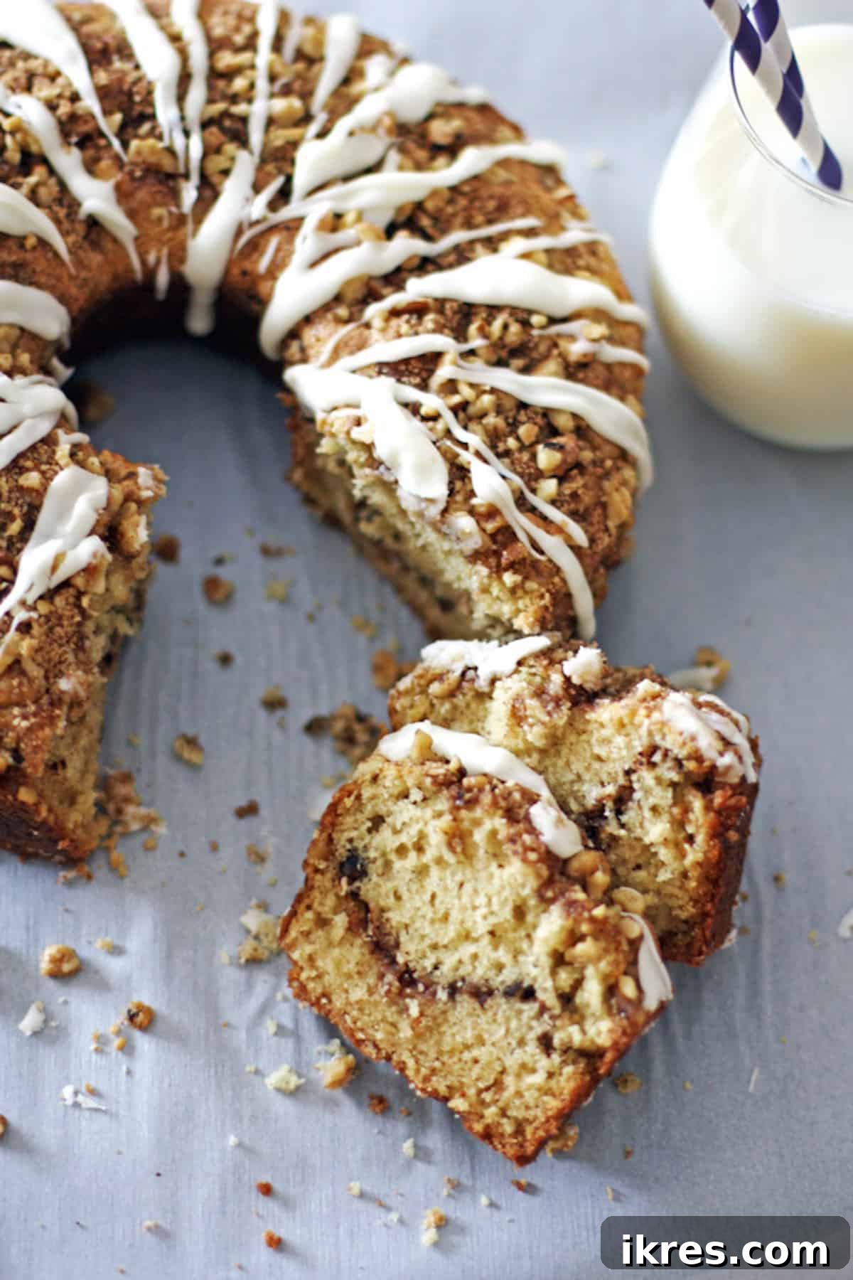 Two slices of glazed cinnamon streusel coffee cake in front of the rest of the cake, showcasing the rich texture and delicious glaze.