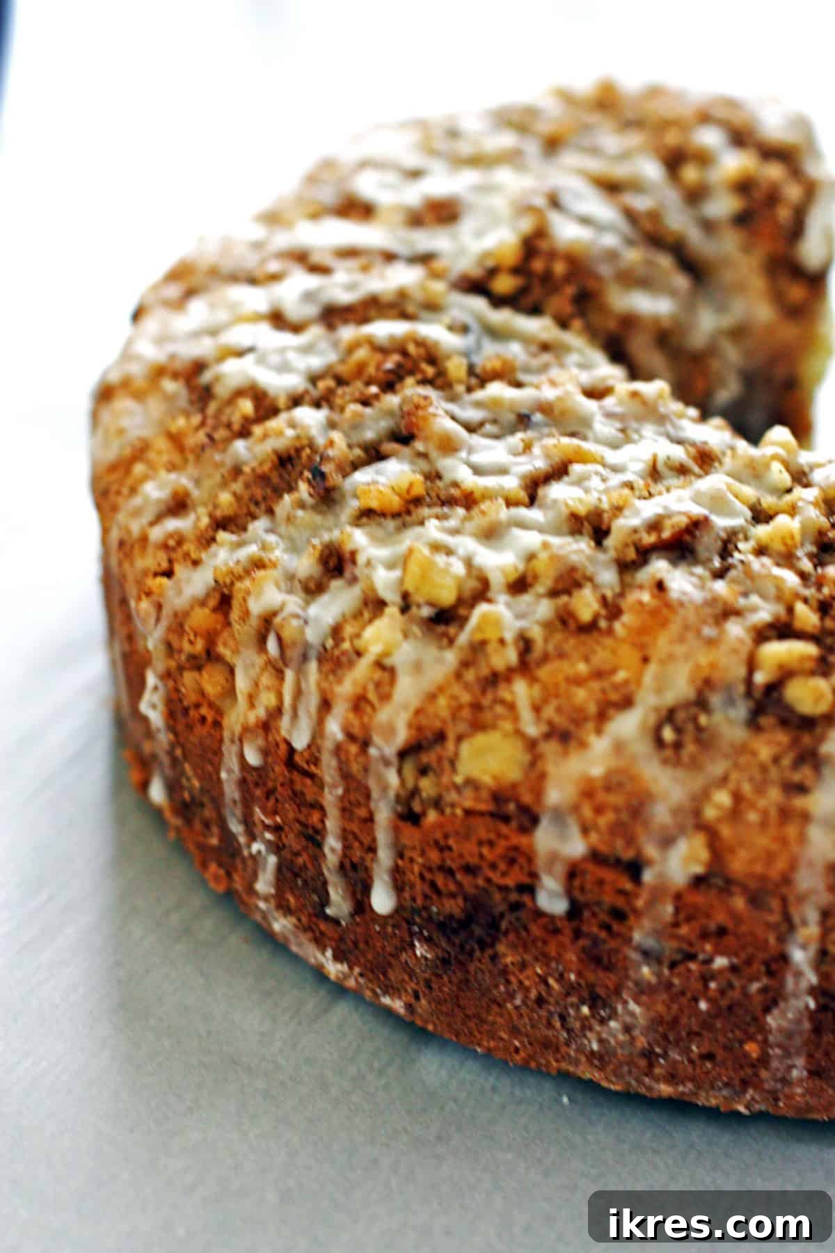 A side view of a cinnamon streusel coffee cake with a thinner glaze dripping down, highlighting its moistness.