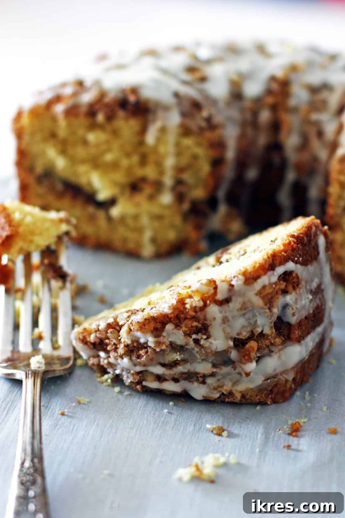 A single slice of cinnamon sour cream coffee cake placed in front of the main cake, showing the thicker glaze and streusel layers.