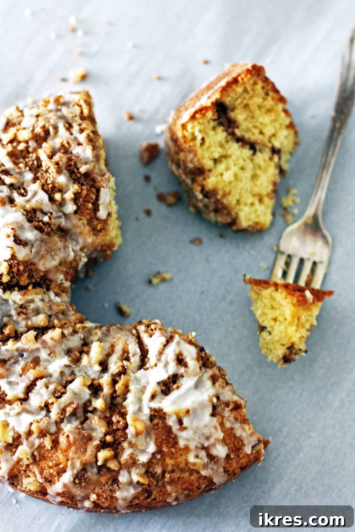 Half of a glazed coffee cake with a bite on a fork and a slice showing a cinnamon streusel layer in the middle, ready to be enjoyed.
