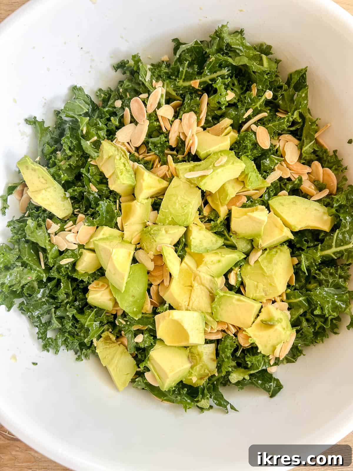 Lemon-Kissed Kale Avocado Salad 8 Diced avocado and crunchy sliced almonds being carefully added to the vibrant massaged kale salad.