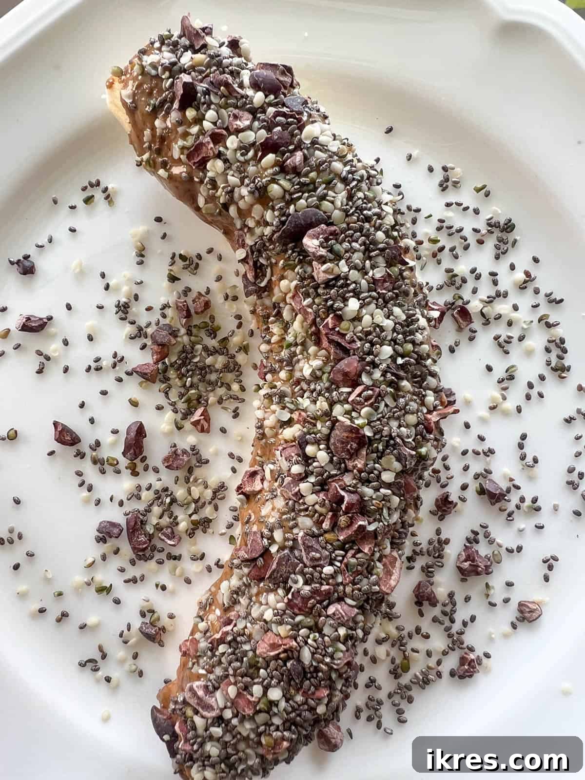 Banana Breakfast Pinwheels 4 A peeled banana covered with a layer of almond butter and a sprinkle of seeds and nibs.