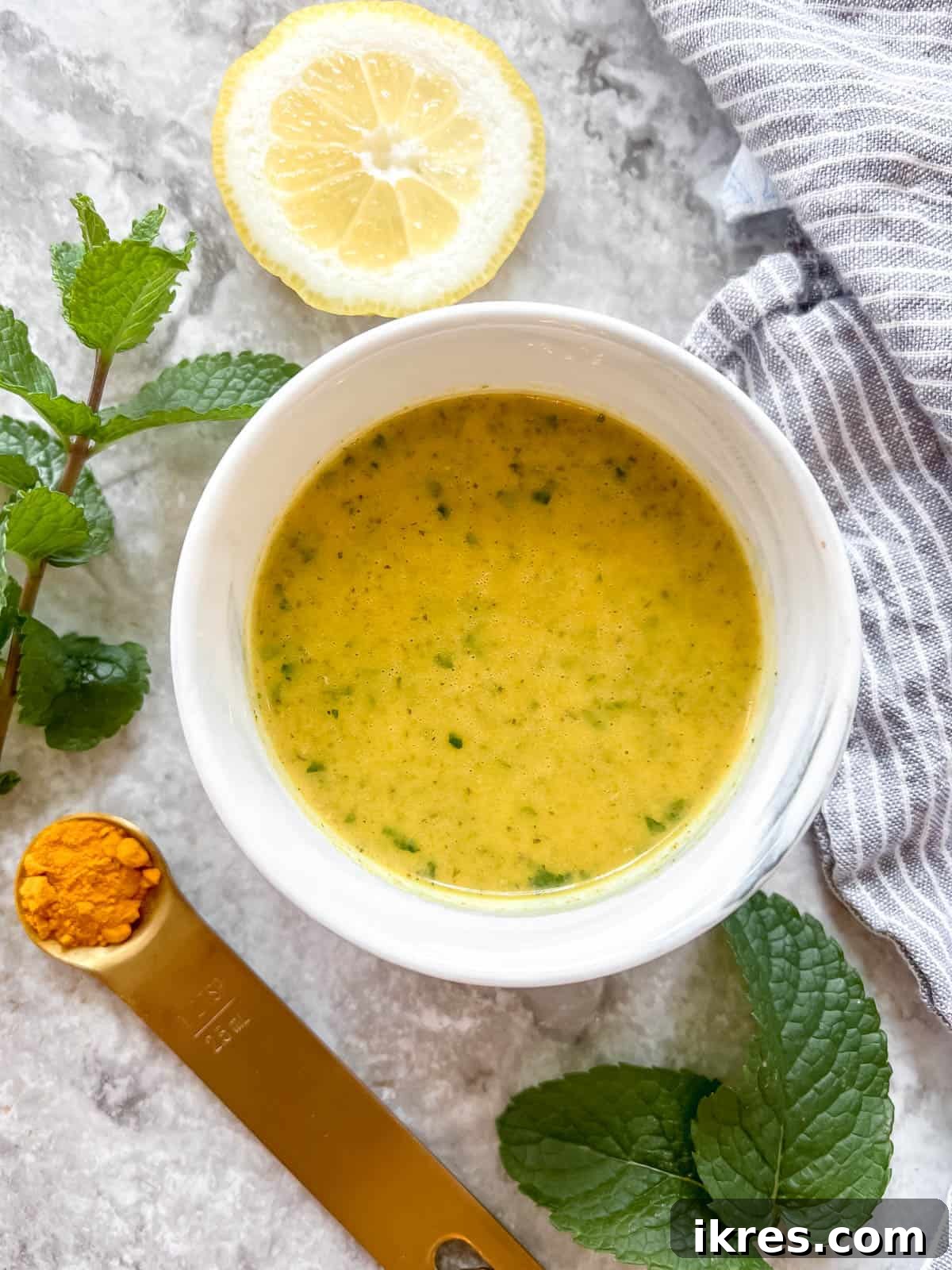 A bowl of vibrant lemon turmeric dressing with fresh mint leaves and turmeric root nearby, highlighting its natural ingredients.