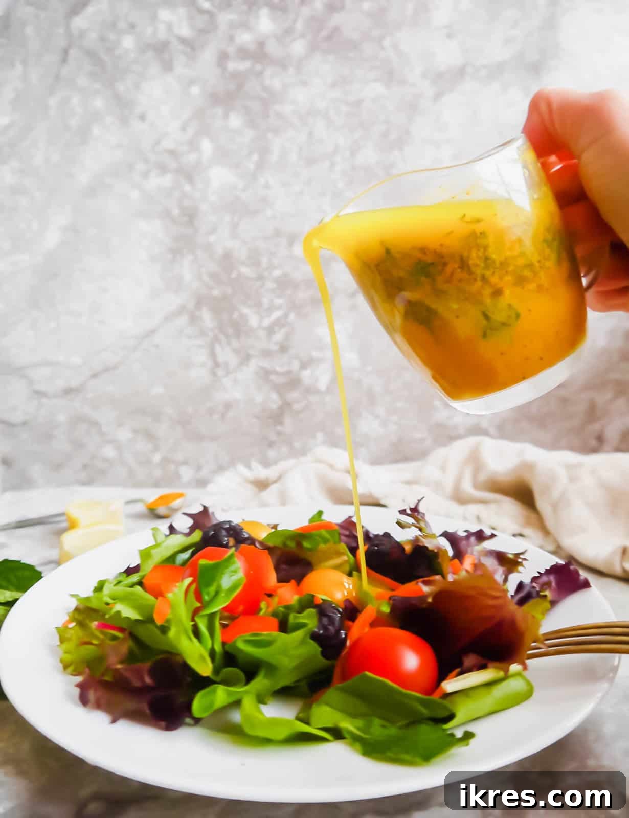 Lemon turmeric dressing with mint being generously poured over a fresh, colorful salad.