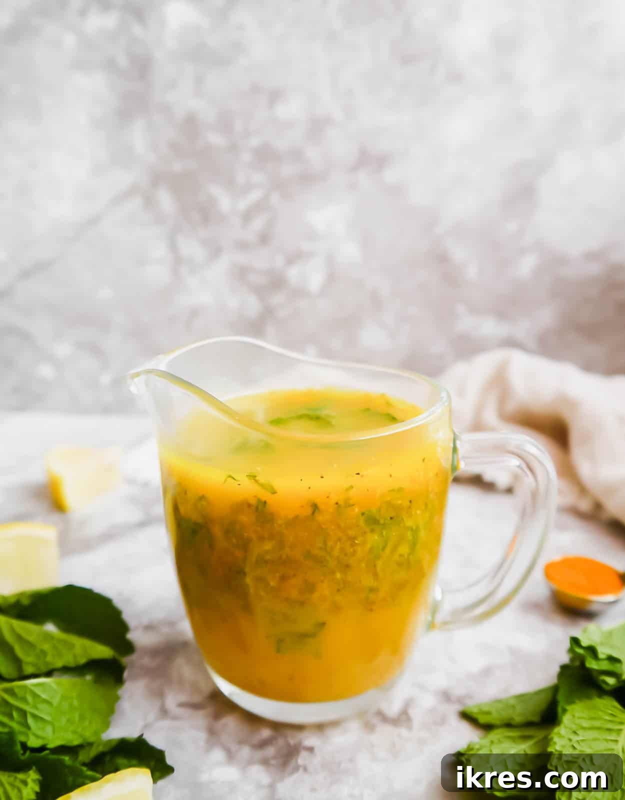 A jar of homemade lemon turmeric mint dressing, sealed and ready for refrigeration, surrounded by fresh ingredients.