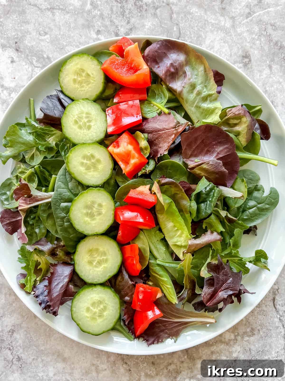 Vibrant Grilled Chicken Greek Salad 11 Diced red bell pepper being gently added to the salad greens and cucumbers, adding color and crunch.