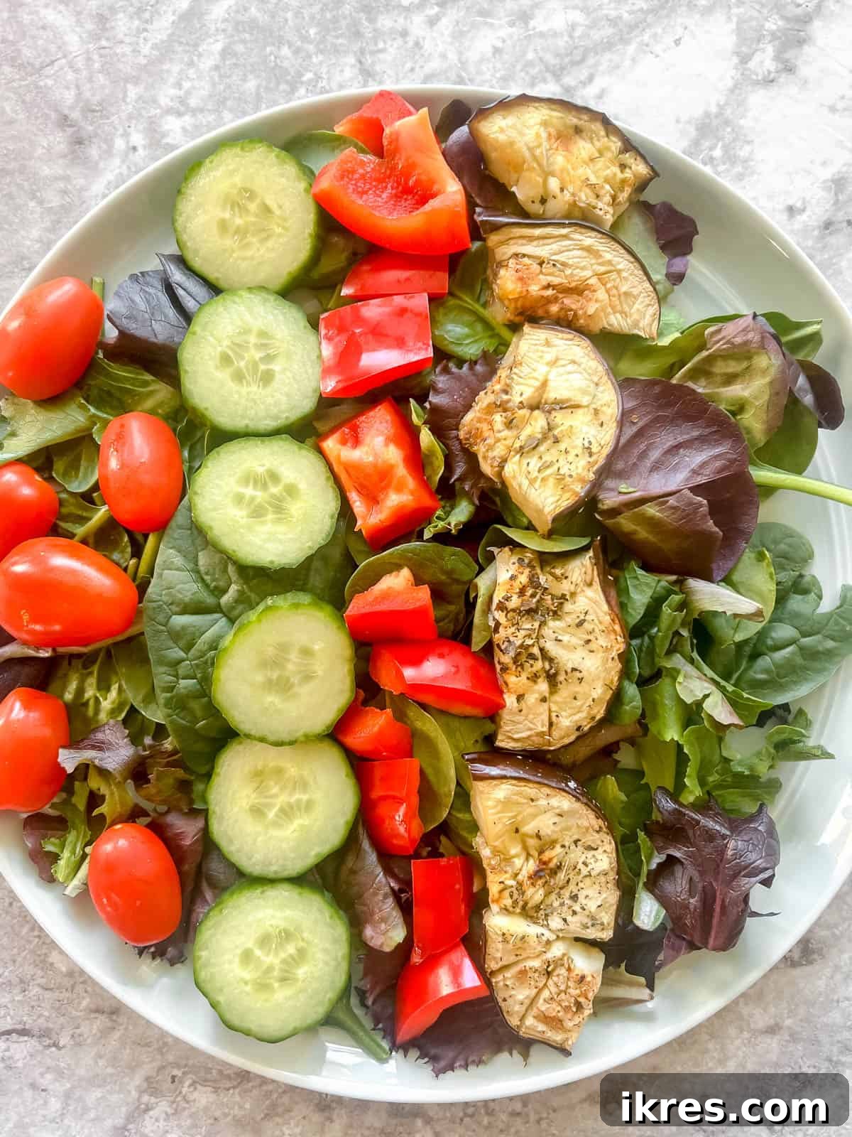 Vibrant Grilled Chicken Greek Salad 12 Juicy cherry tomatoes and tender roasted eggplant pieces being placed into the salad.