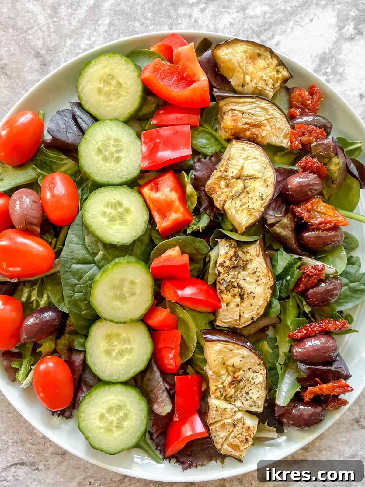 Vibrant Grilled Chicken Greek Salad 13 Kalamata olives and sliced sun-dried tomatoes being added as key Mediterranean elements to the salad.