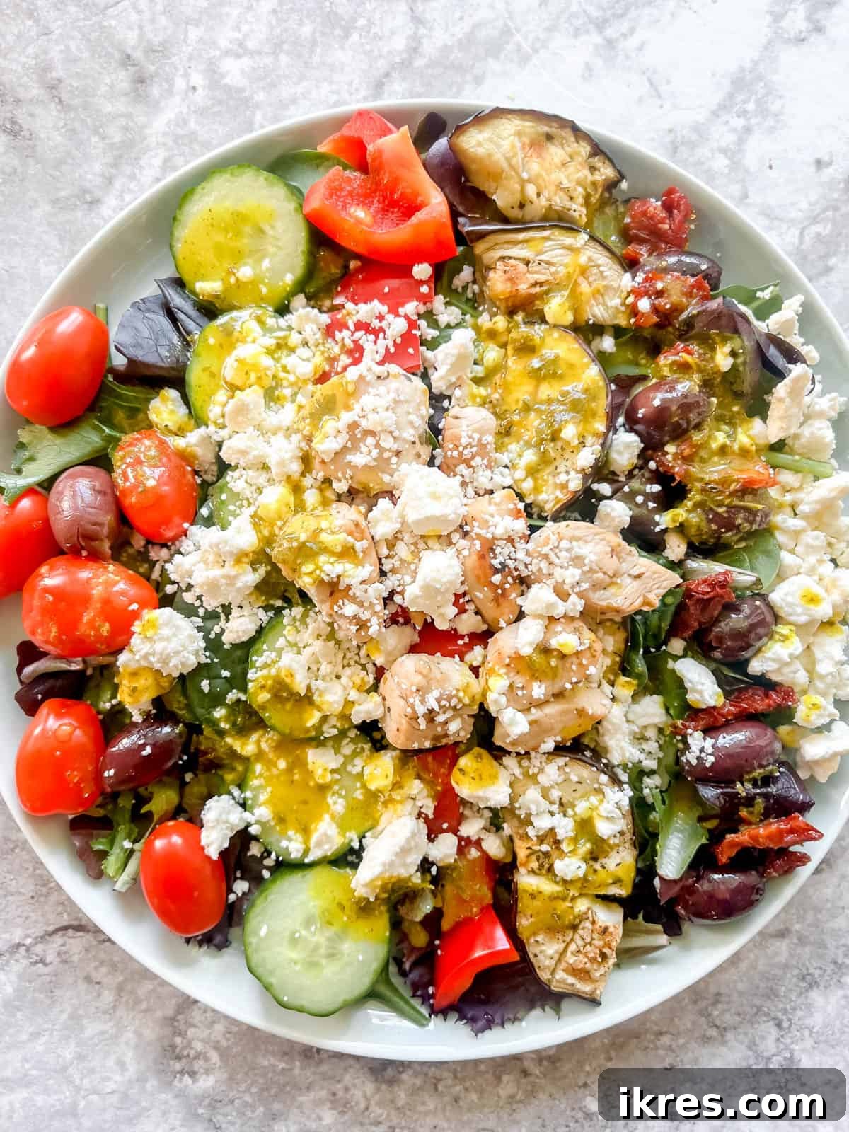 Vibrant Grilled Chicken Greek Salad 15 Crumbled feta cheese and a light drizzle of vibrant dressing completing the Greek salad, ready to be tossed and served.