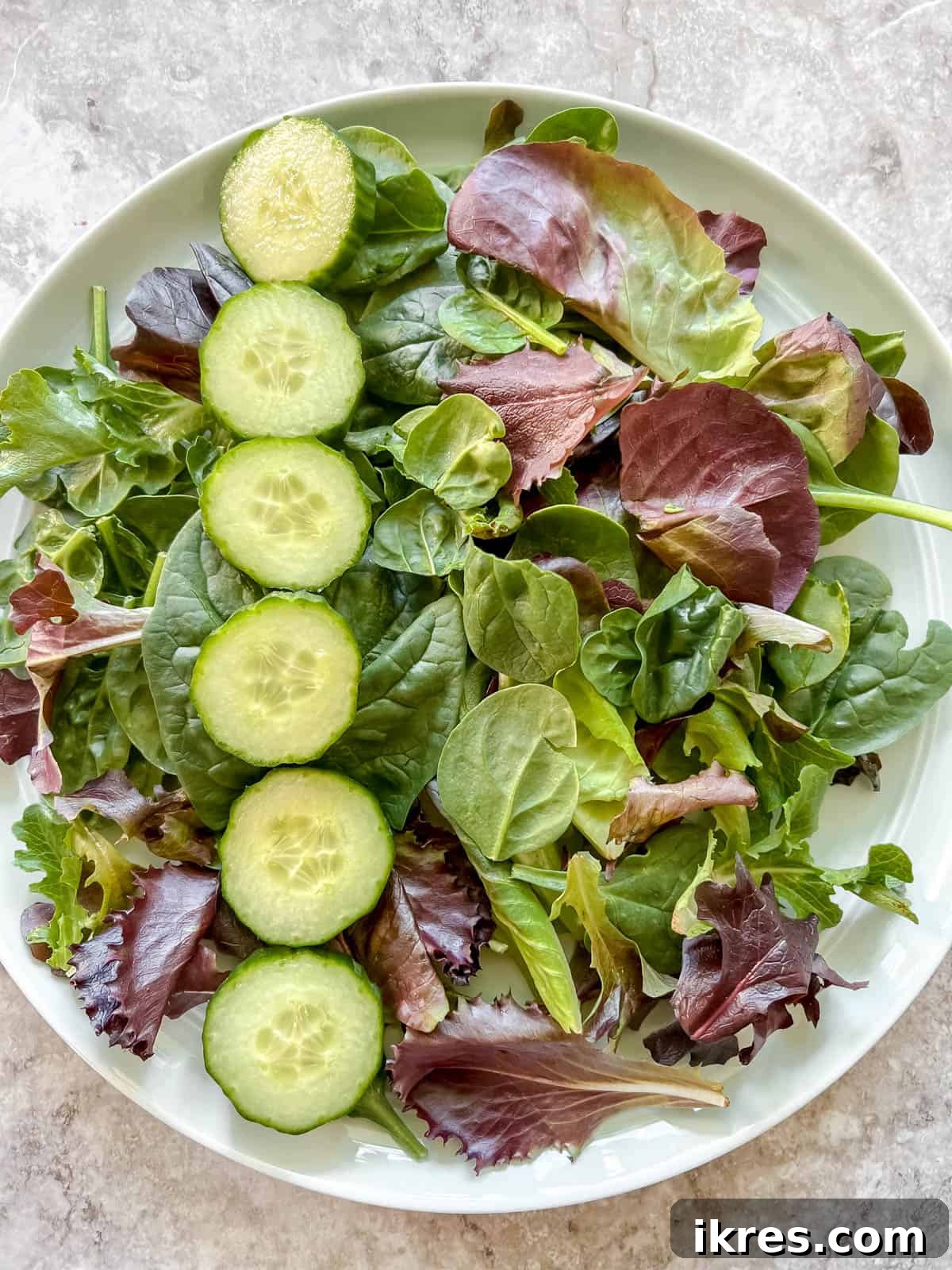 Vibrant Grilled Chicken Greek Salad 10 Freshly sliced cucumber being added to a bed of mixed salad greens in a serving bowl.