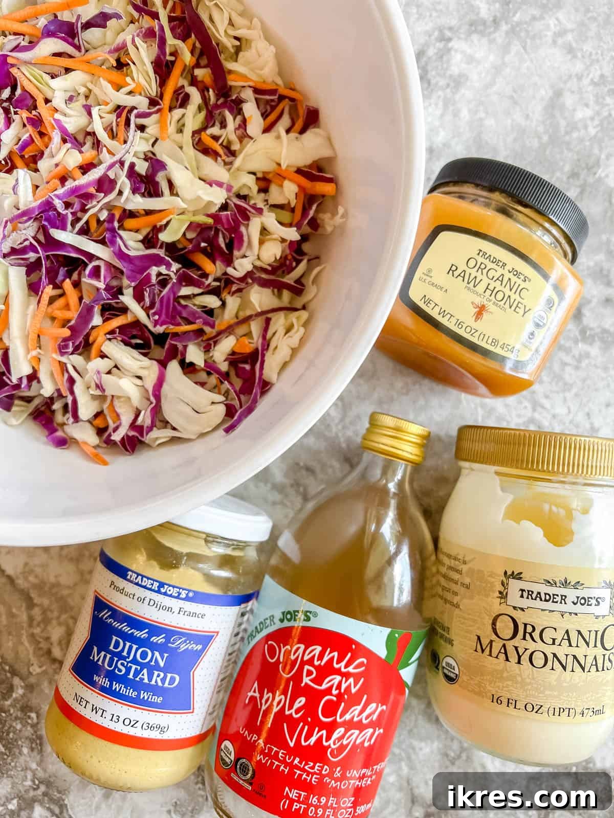 Ingredients laid out on a counter to make Paleo coleslaw, including a bag of cabbage mix, mayonnaise, honey, apple cider vinegar, and mustard.