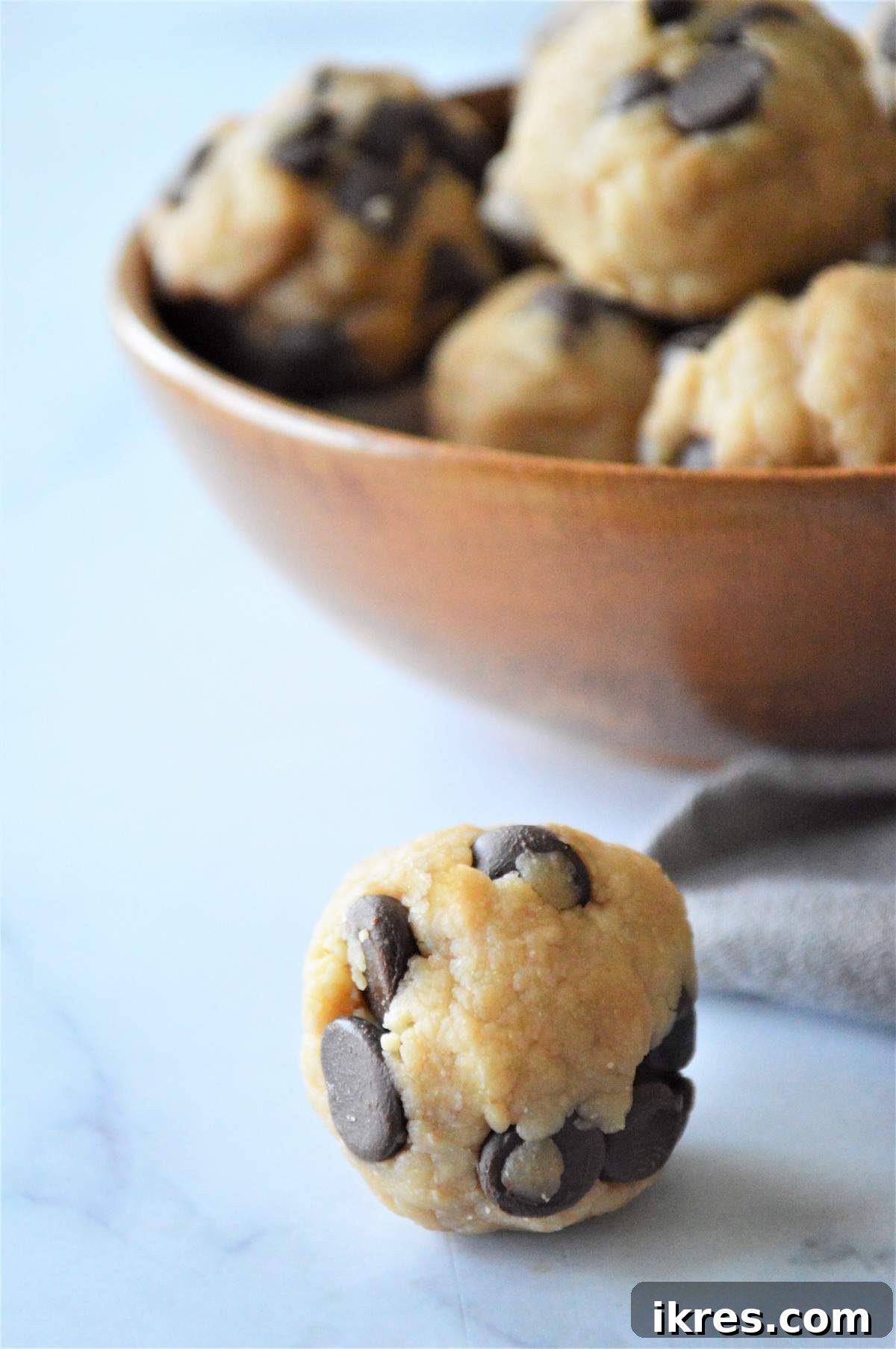 Easy No-Bake Power Bites 11 A single no-bake cookie dough energy bite in the foreground, with a blurred bowl of more bites behind it, highlighting its tempting texture.