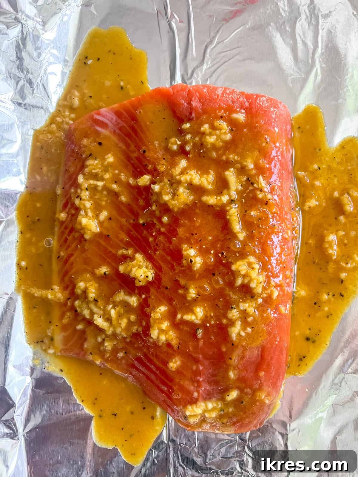 Salmon fillet placed on aluminum foil with the turmeric ginger sauce poured over it.
