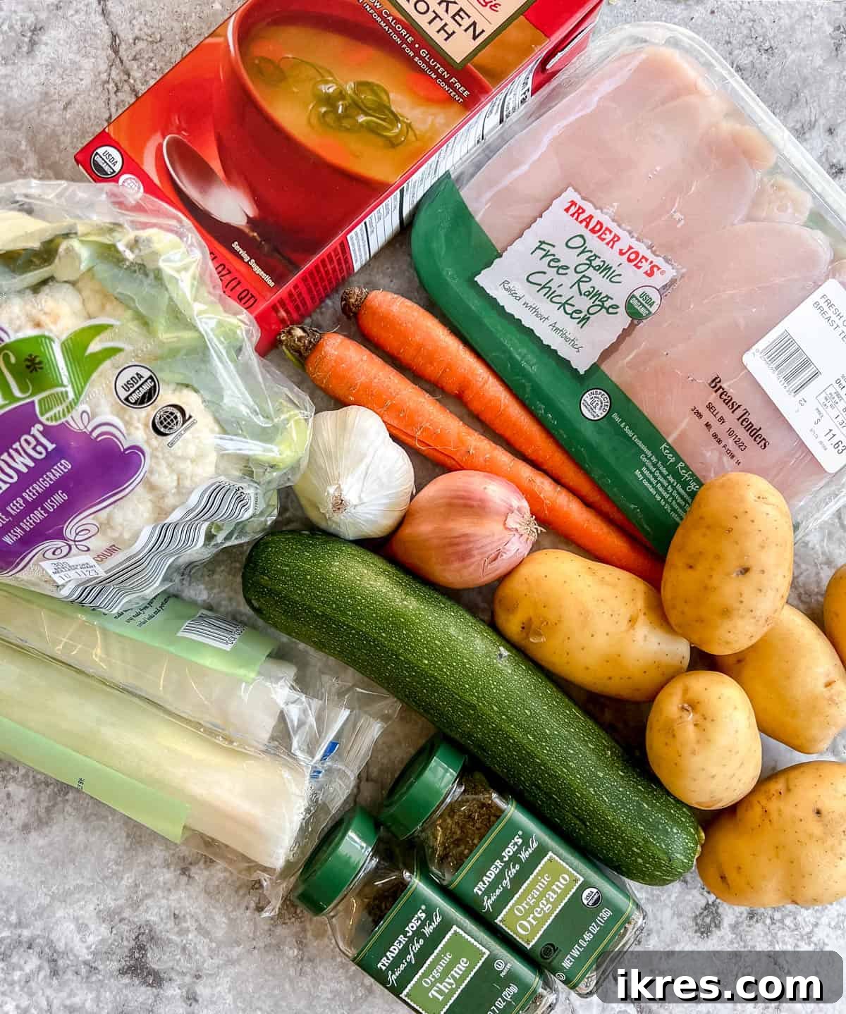 A selection of fresh vegetables including shallots, garlic, leeks, carrots, potatoes, cauliflower, and zucchini, alongside chicken tenders and chicken broth, laid out for making chicken and leek soup.