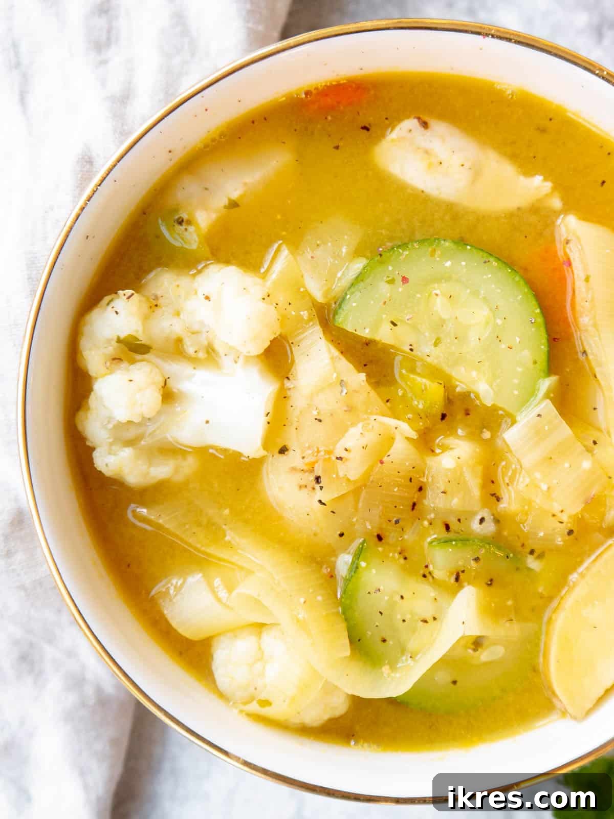 Close-up of a bowl of chicken leek soup, showing tender pieces of chicken, carrots, potatoes, cauliflower, and zucchini in a rich, herby broth.