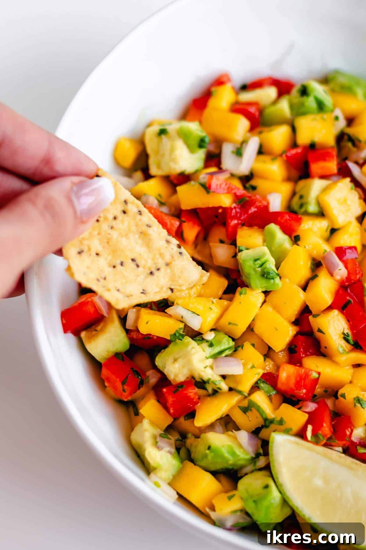 Tropical Mango Avocado Salsa 2 A tortilla chip generously scooping vibrant homemade mango avocado salsa from a white bowl, showcasing the fresh diced ingredients.