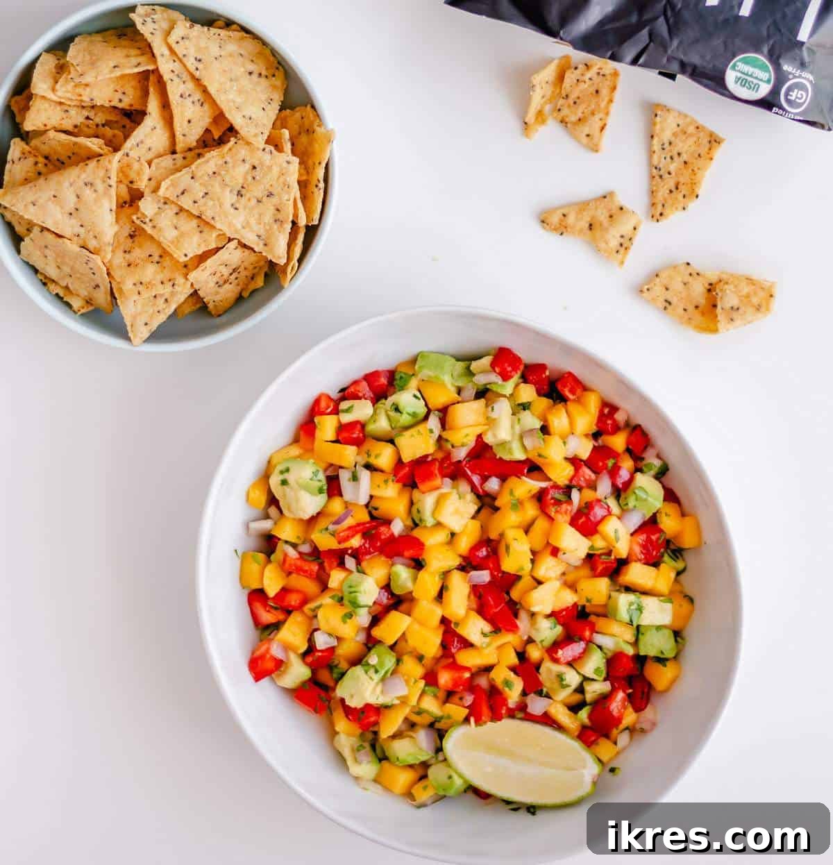 Tropical Mango Avocado Salsa 7 A large bowl of vibrant homemade mango and avocado salsa next to a smaller bowl overflowing with crispy tortilla chips, inviting you to dig in.