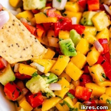 A chip scooping homemade mango avocado salsa out of a bowl, highlighting its vibrant texture.