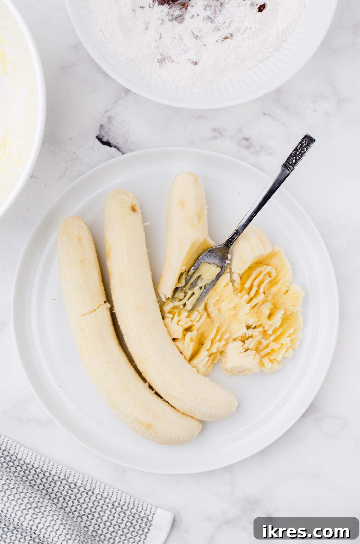 Buttermilk Banana Bread Perfection 6 Perfectly mashed ripe bananas, a vibrant golden color, are presented on a white plate, ready to be incorporated into the buttermilk banana bread batter.