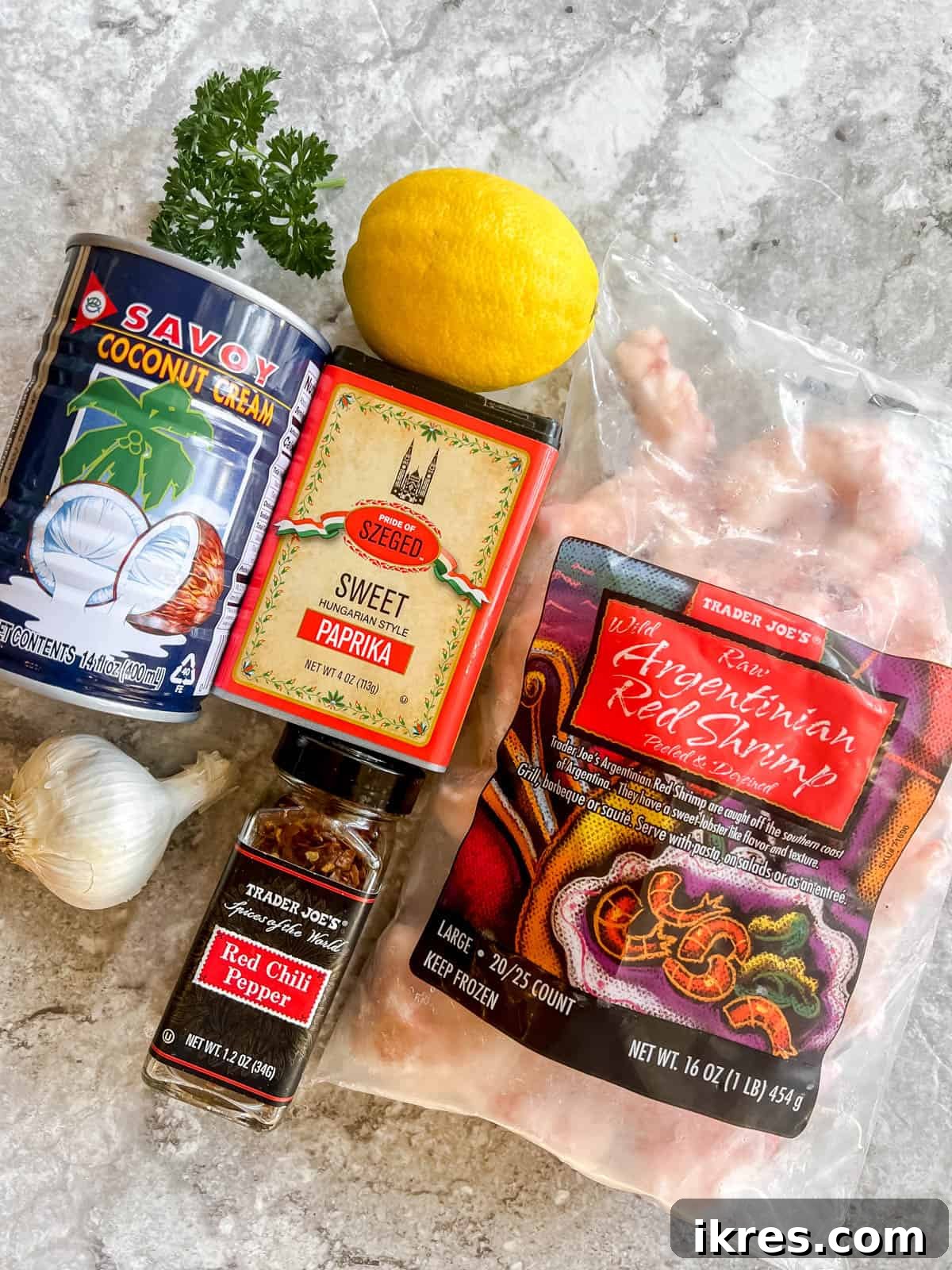 Ağızda Dağılan Paleo Paprika Sarımsaklı Karides 4 A selection of fresh ingredients laid out: garlic cloves, paprika spice, canned coconut cream, fresh lemon, parsley, raw shrimp, crushed red pepper flakes, and coconut oil.
