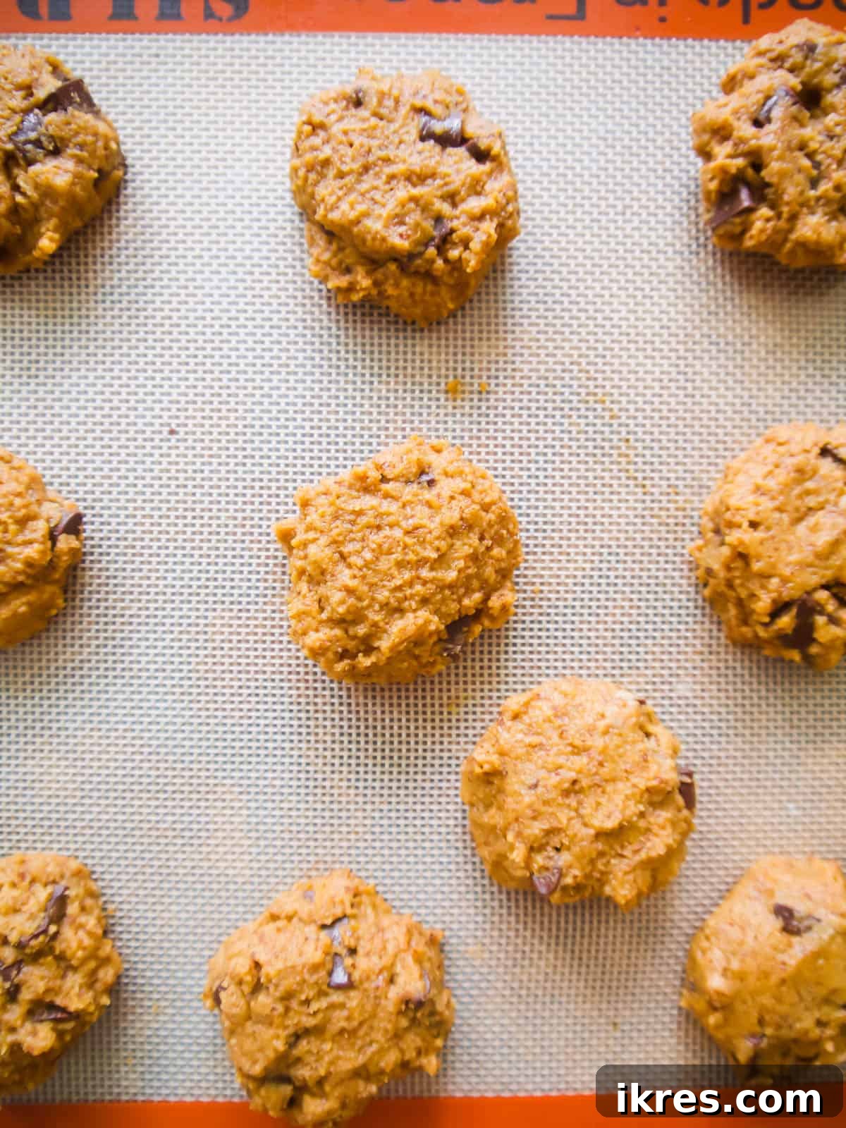 Grain-Free Pumpkin Spice Cookies 4 Raw cookie dough balls of healthy pumpkin chocolate chip cookies placed on a baking sheet, ready for the oven.