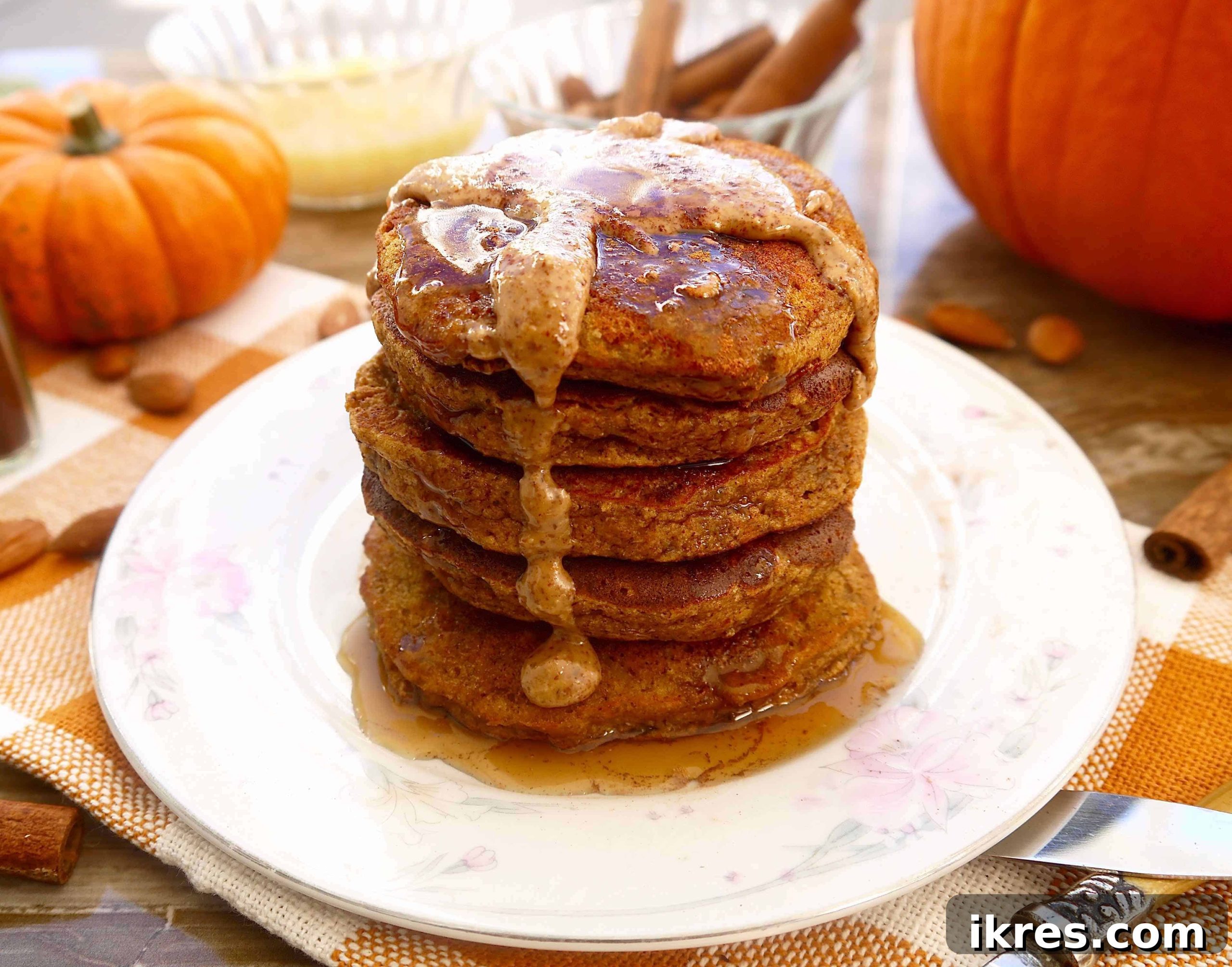 Stacks of golden-brown Paleo Pumpkin Pancakes on a white plate, drizzled with maple syrup and garnished with a sprinkle of cinnamon, ready to be enjoyed.