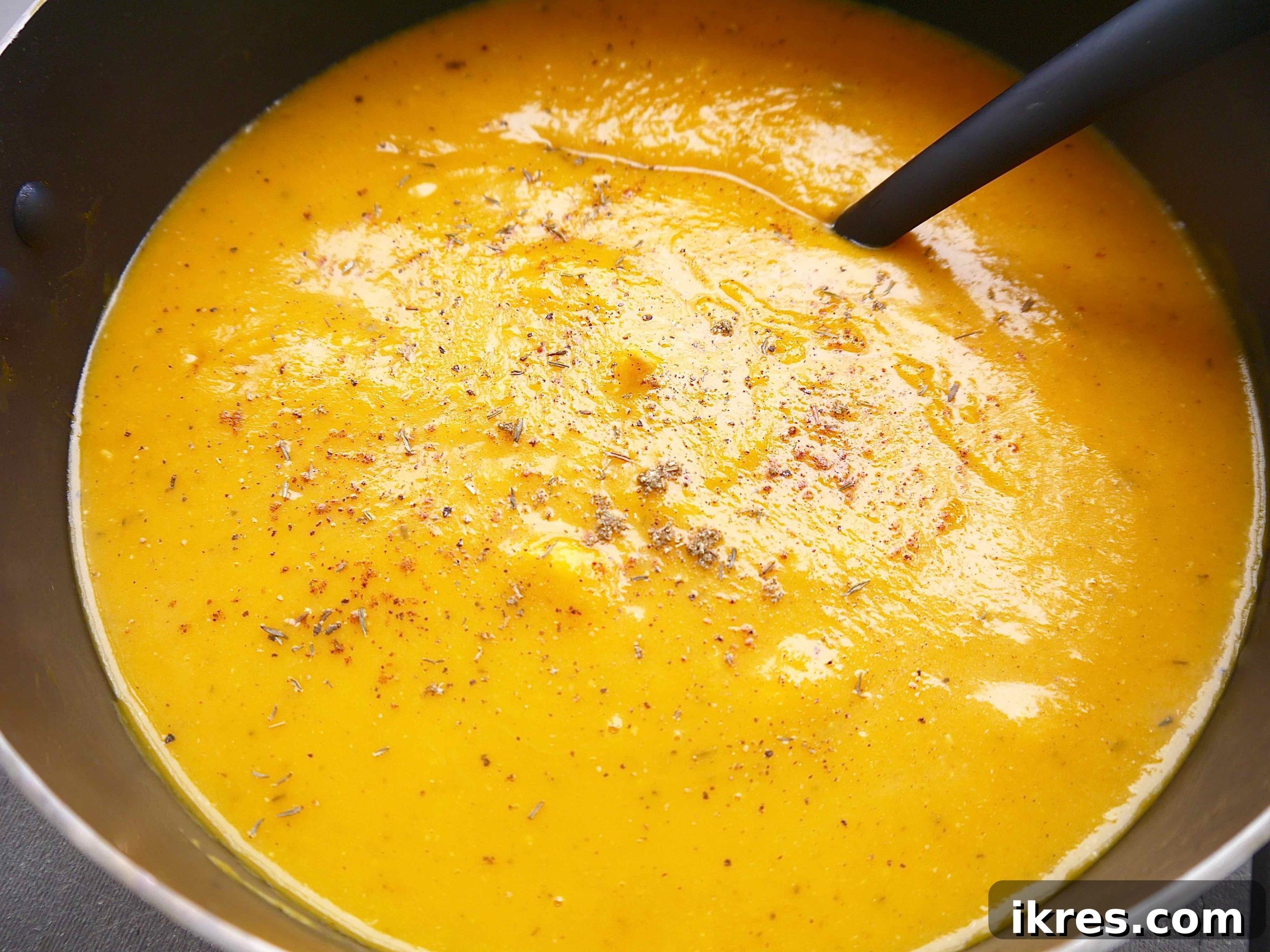 Butternut squash soup being pureed with an immersion blender in a large pot.