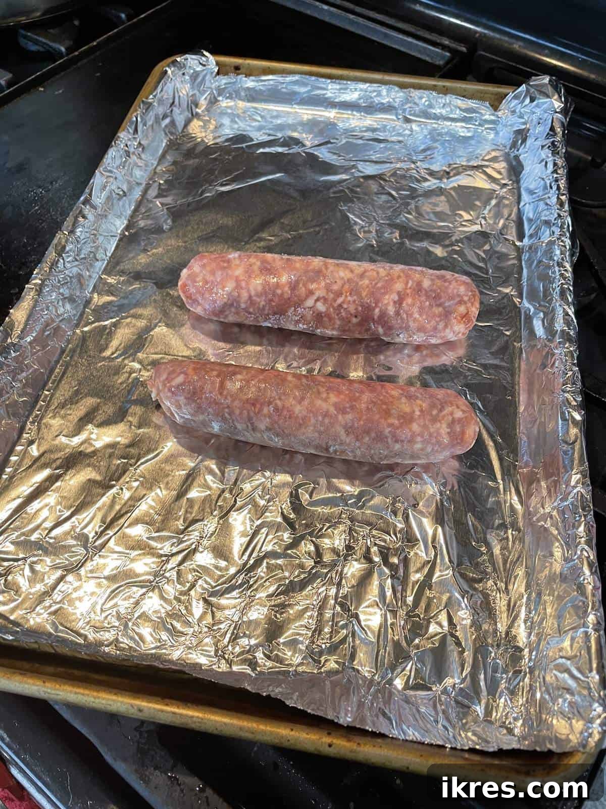 Perfect Oven-Roasted Italian Sausage 2 Two uncooked Italian sausage links on a foil lined baking sheet.