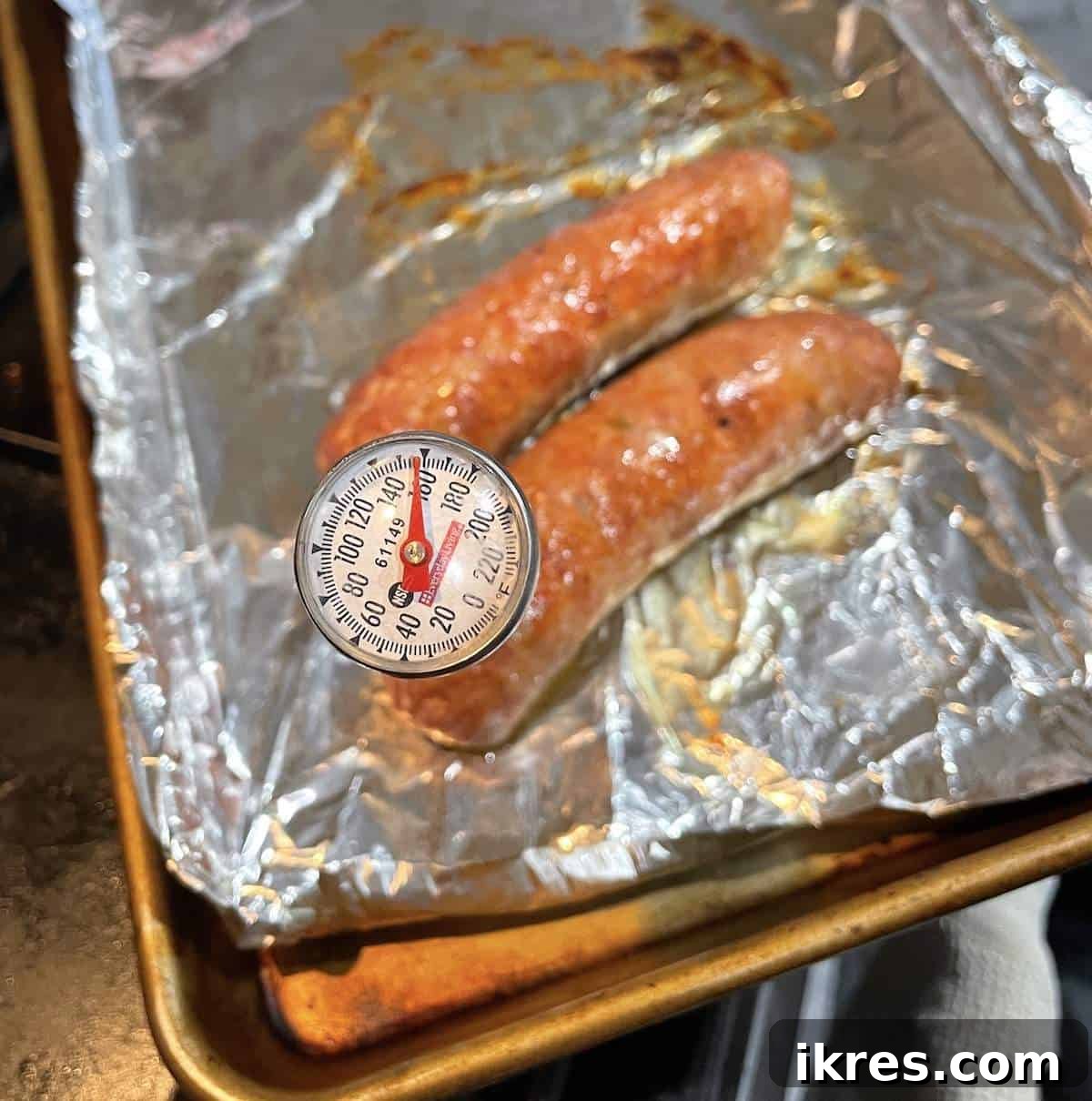 Perfect Oven-Roasted Italian Sausage 5 Two oven baked Italian sausages on a foil lined baking sheet with the temperature being taken.