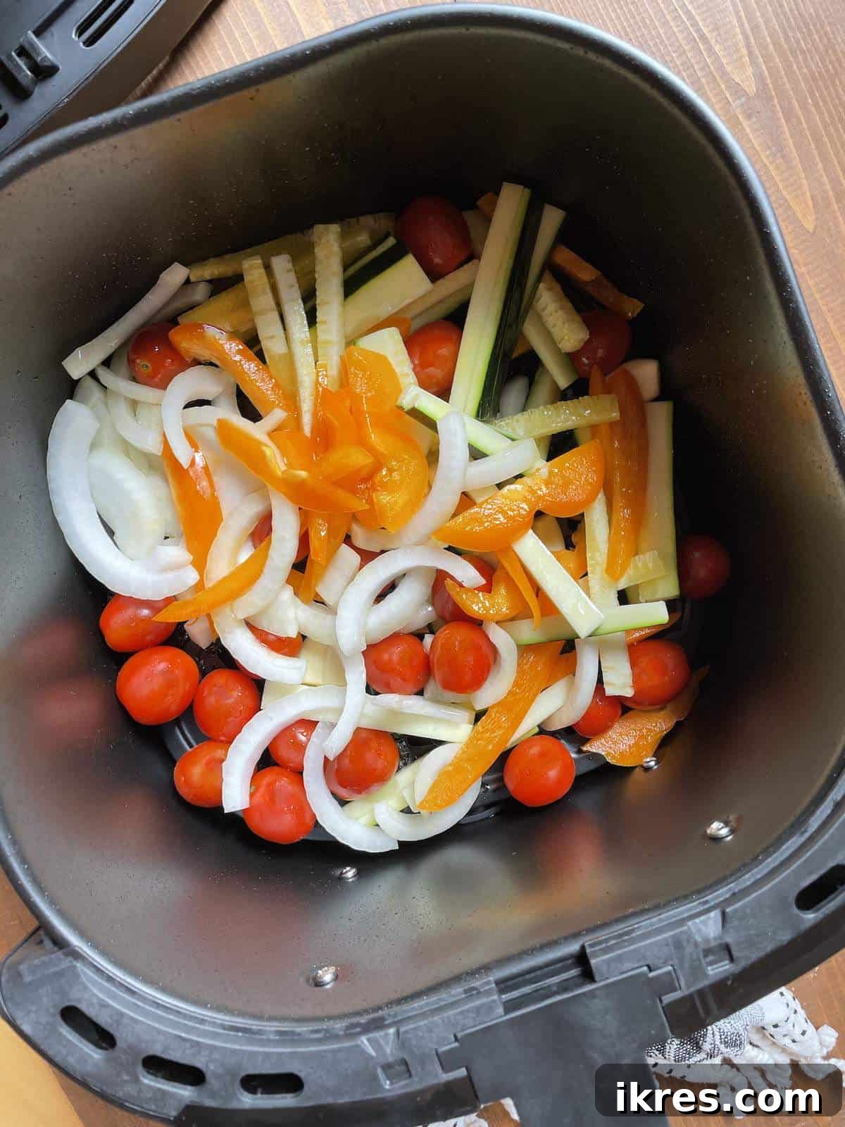 Air Fryer Italian Sausage Perfection 7 Peppers, onions, zucchini, and tomatoes cooking in an air fryer basket.