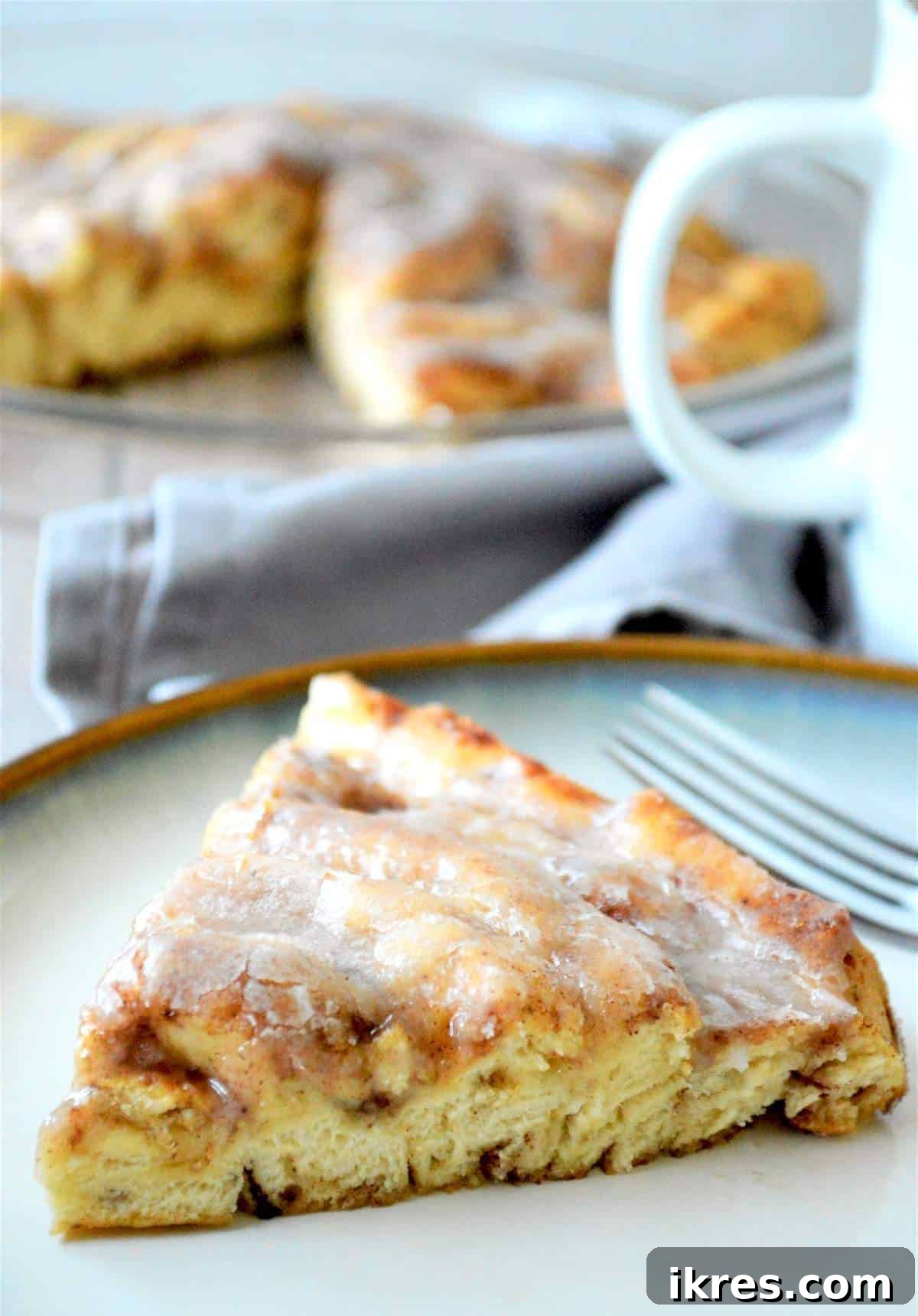 A slice of a giant fluffy cinnamon roll on a plate, showcasing its soft, swirled interior and sweet glaze.