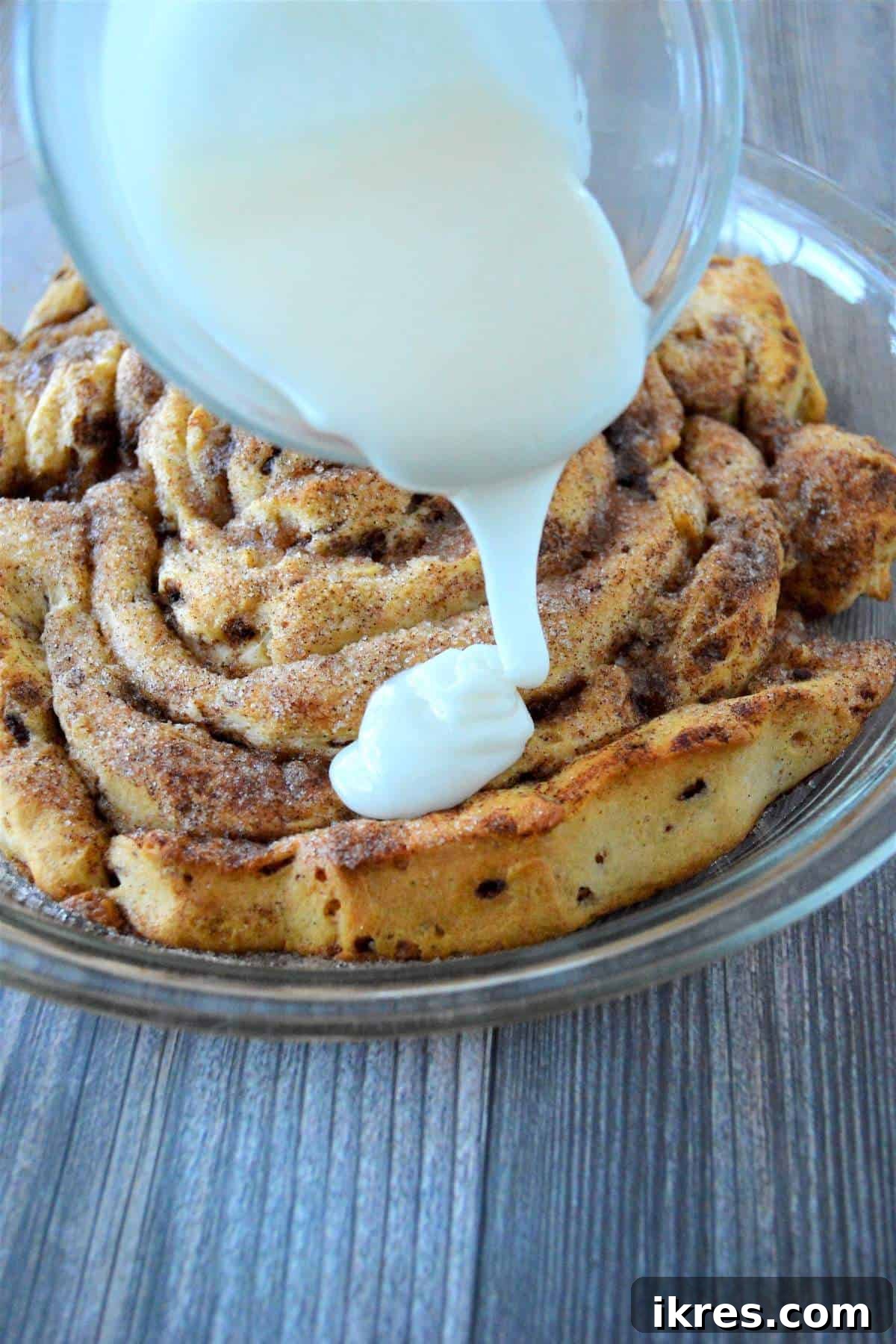Warm cream cheese glaze being generously poured over the freshly baked giant fluffy cinnamon roll.